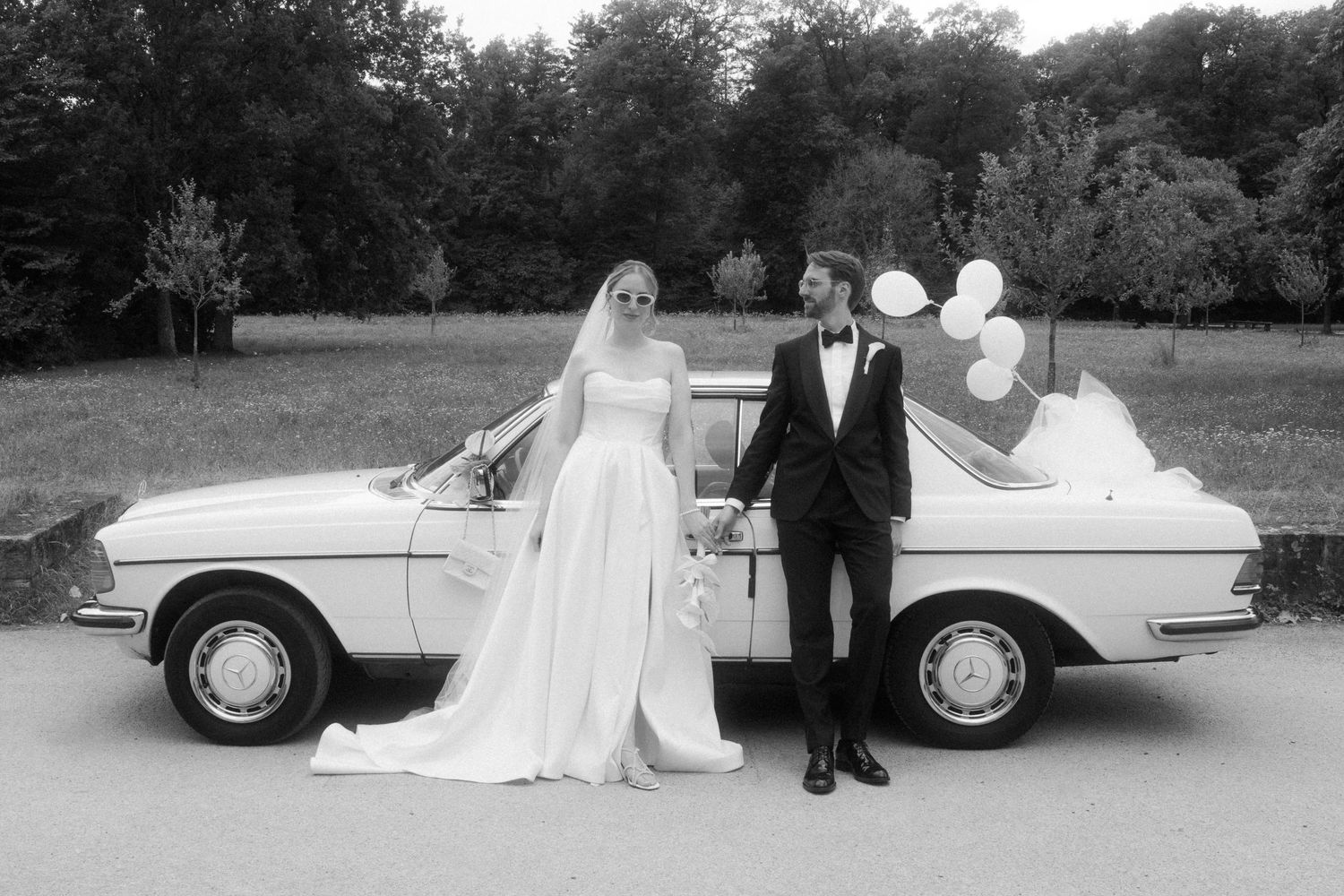 Wedding couple takes romantic photos with vintage car in black and white.