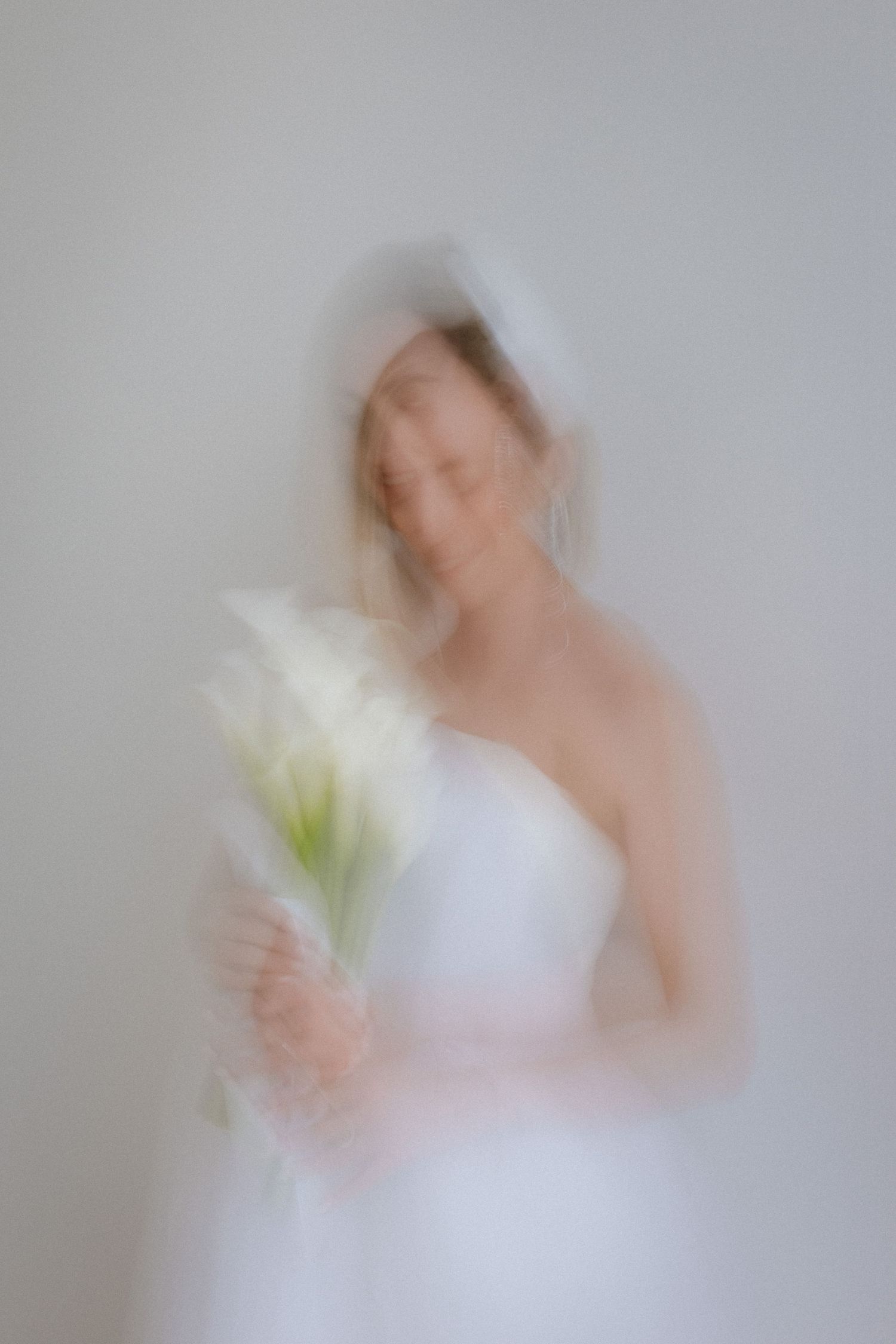 Artistic blurred photo of bride in white dress holding calla lilies.