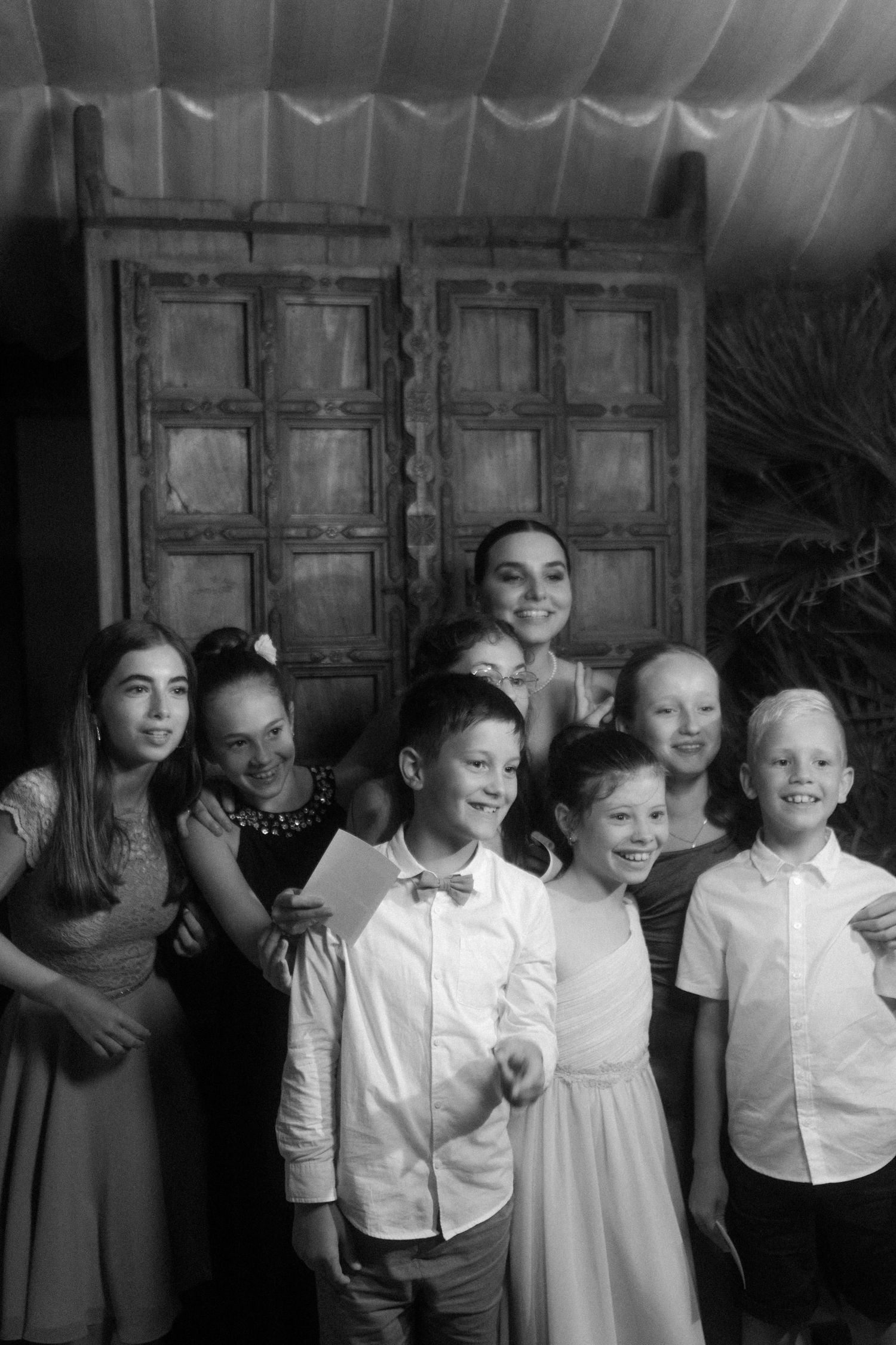 Group photo of children and adults against wooden door backdrop at wedding celebration.