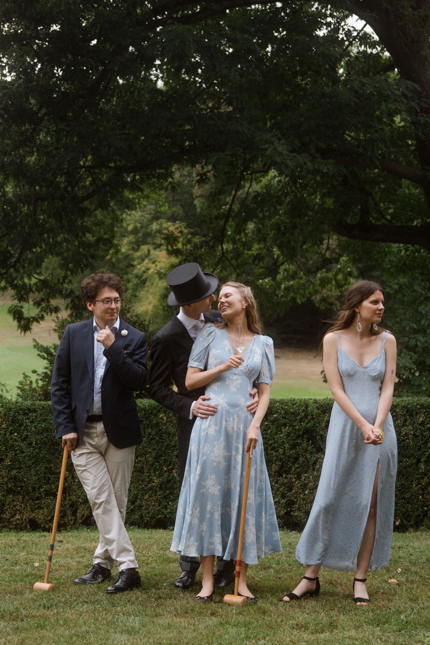 Wedding party members in formal attire playing croquet on a sunny lawn.