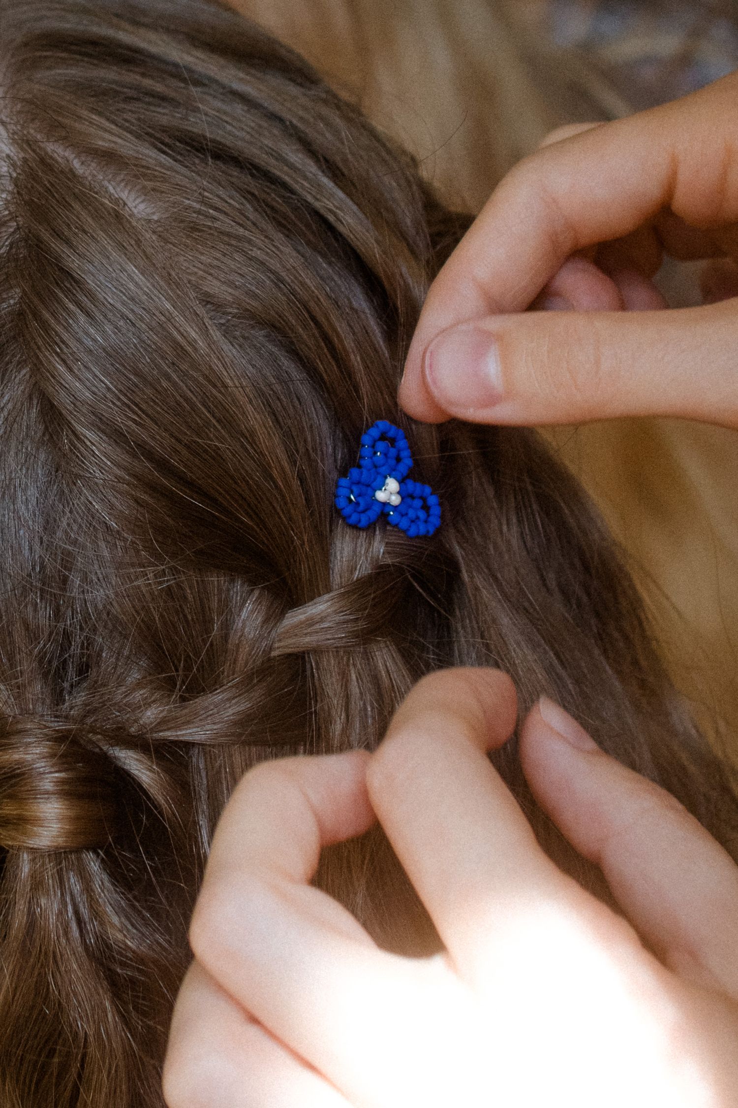 Close-up of hands placing small blue hair accessories in brown hair.