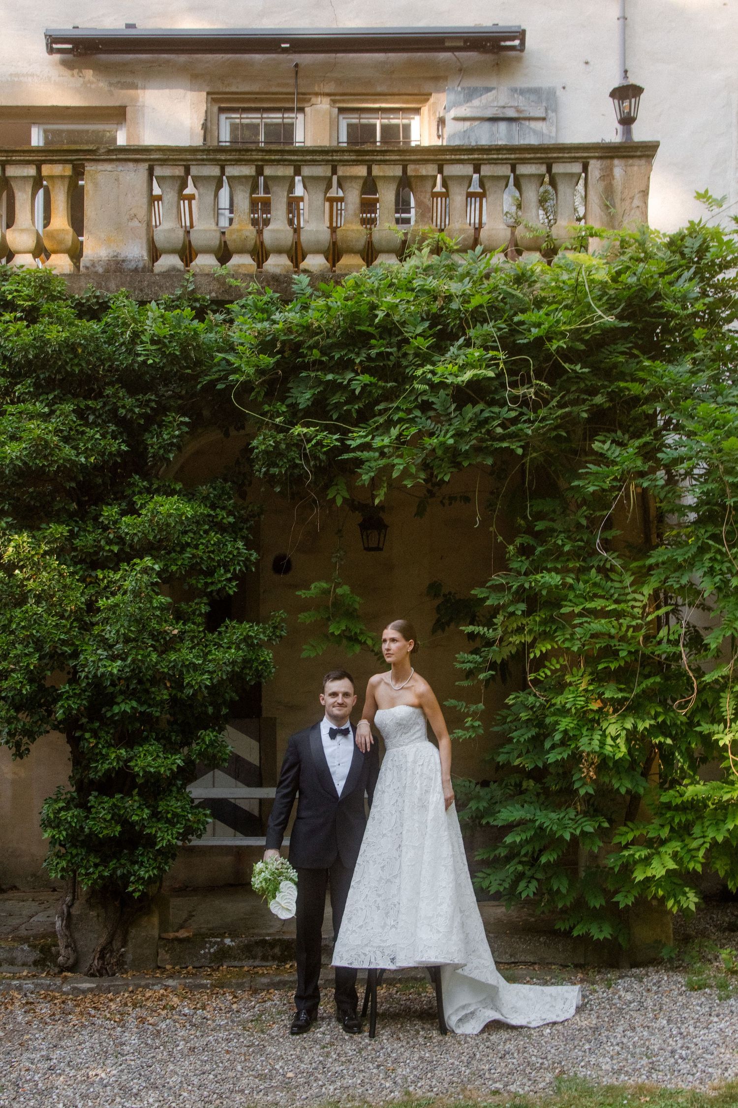 Bride and groom posing in front of ivy-covered villa balustrade on their wedding day.
