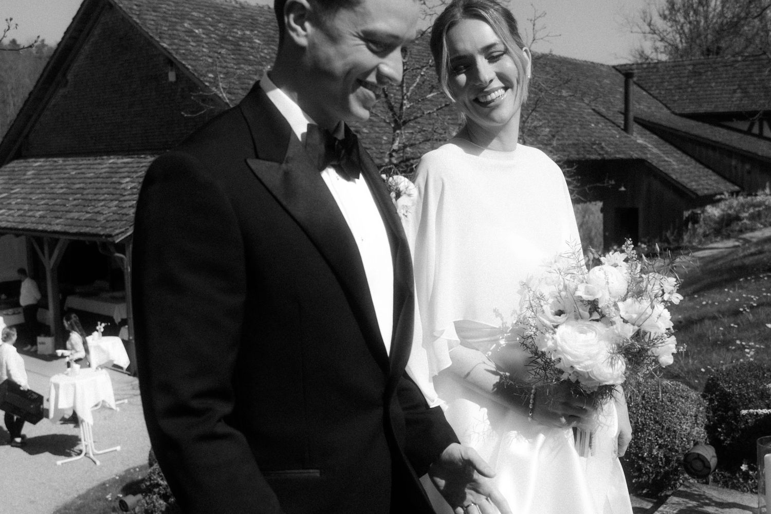 Black and white photo of smiling bride and groom with bouquet at outdoor wedding venue.