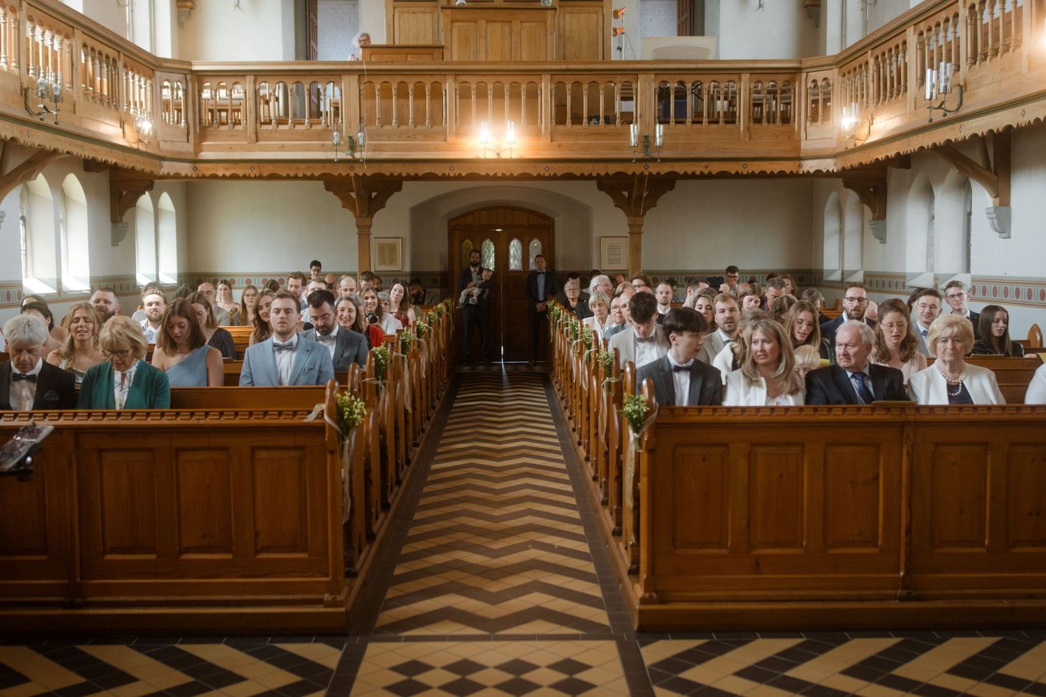 Panoramic view of a church interior filled with wedding guests in wooden pews.