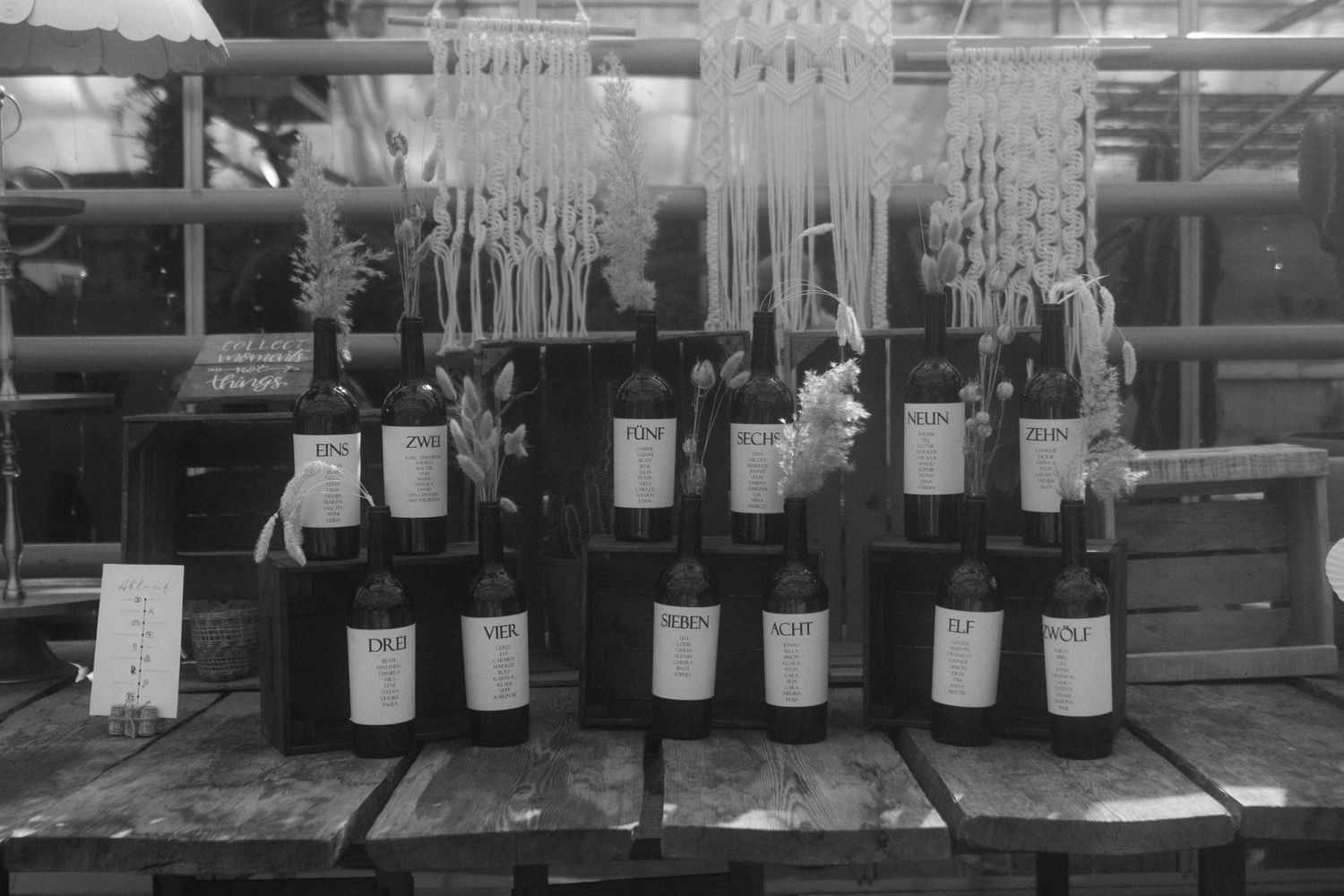 Black and white photo of wine bottles arranged with hanging macrame decorations.