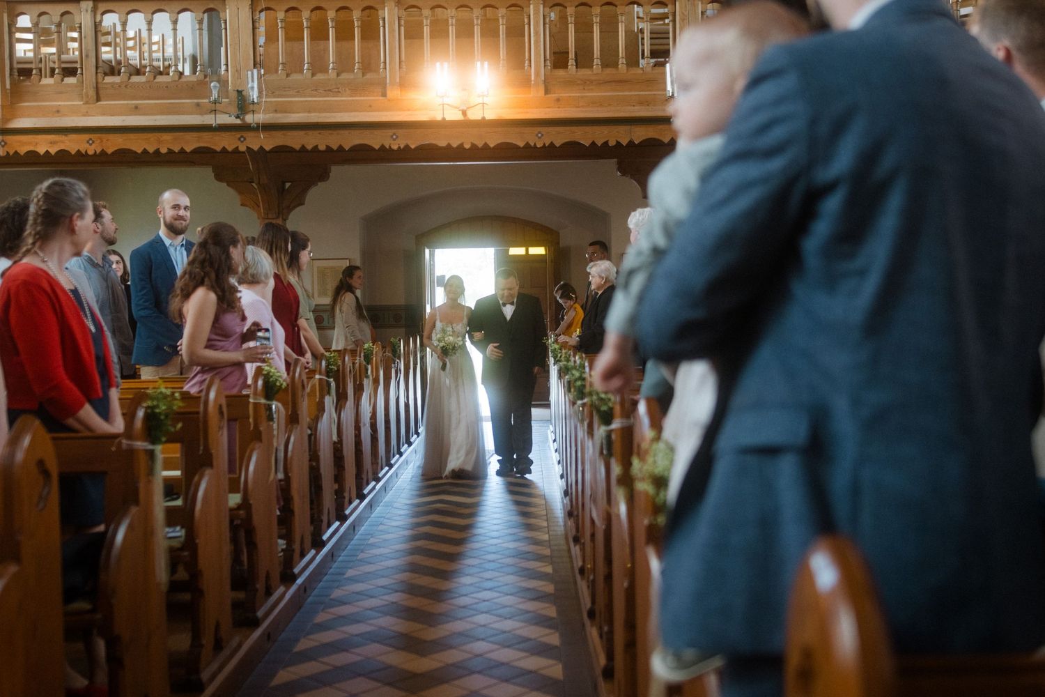 Sunlight streams through church windows as wedding guests gather in wooden pews.