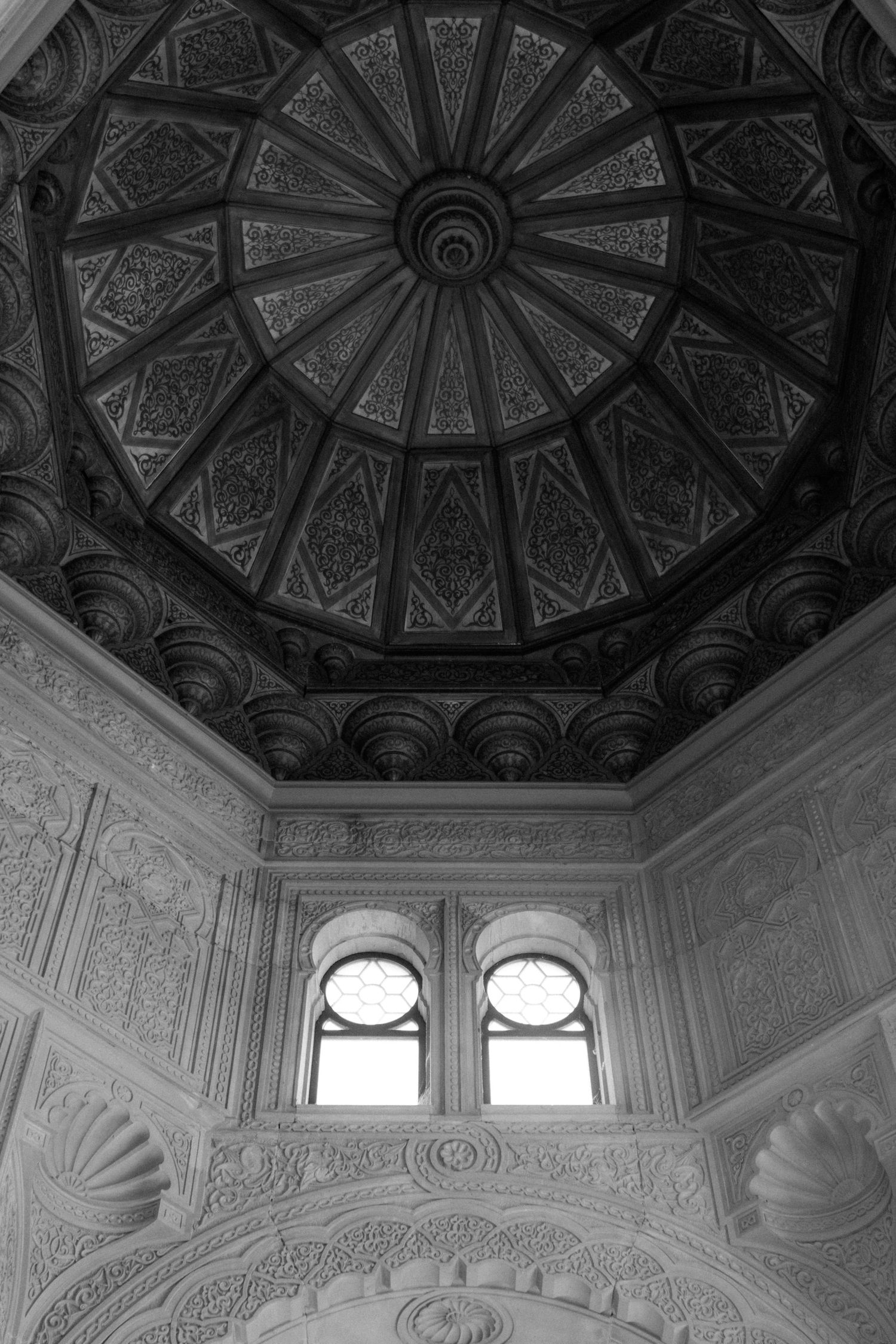 Ornate architectural detail of a domed ceiling with geometric patterns and arched windows in black and white.