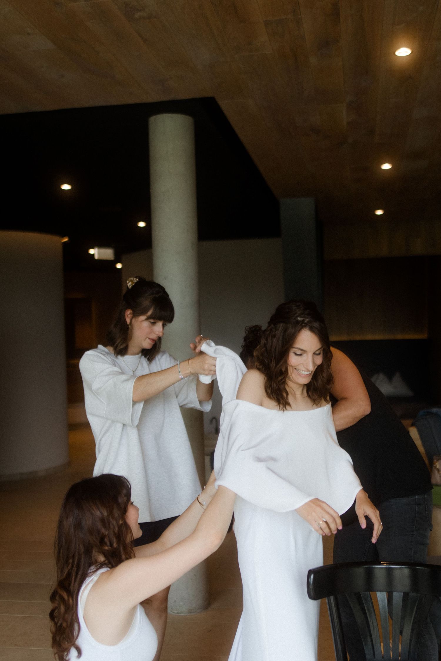 Bridesmaids helping the bride get dressed in a modern room with columns and recessed lighting.