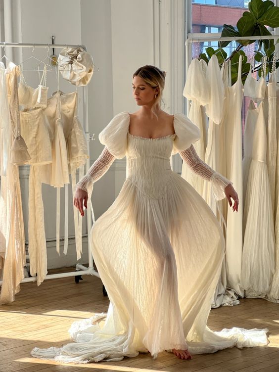 A flowy white wedding dress with sheer fabric and puff sleeves displayed in a bridal boutique with natural lighting.