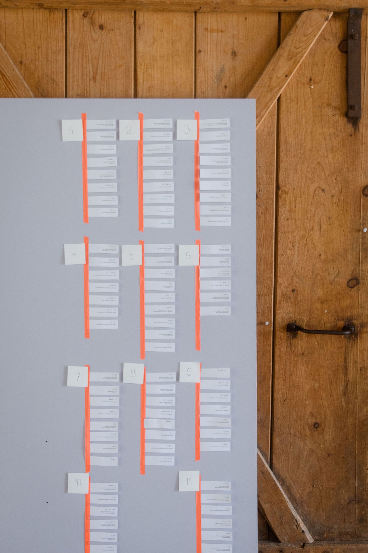 Wedding seating chart displayed on grey board with coral accents and organized name cards.