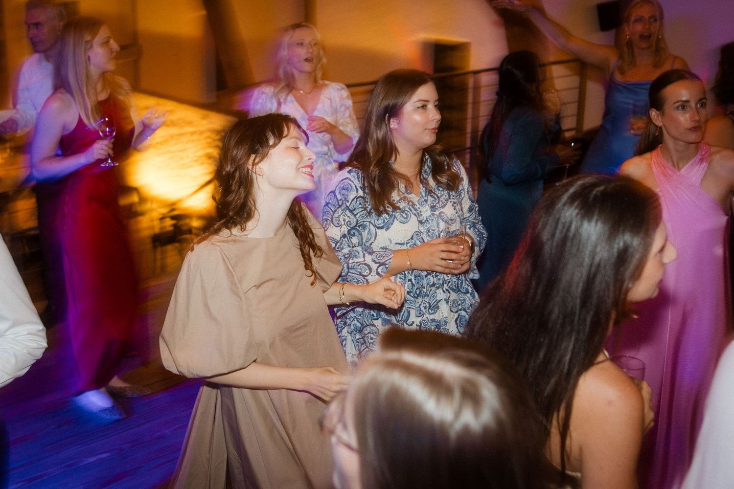 Party guests dancing and celebrating on a colorfully lit dance floor.