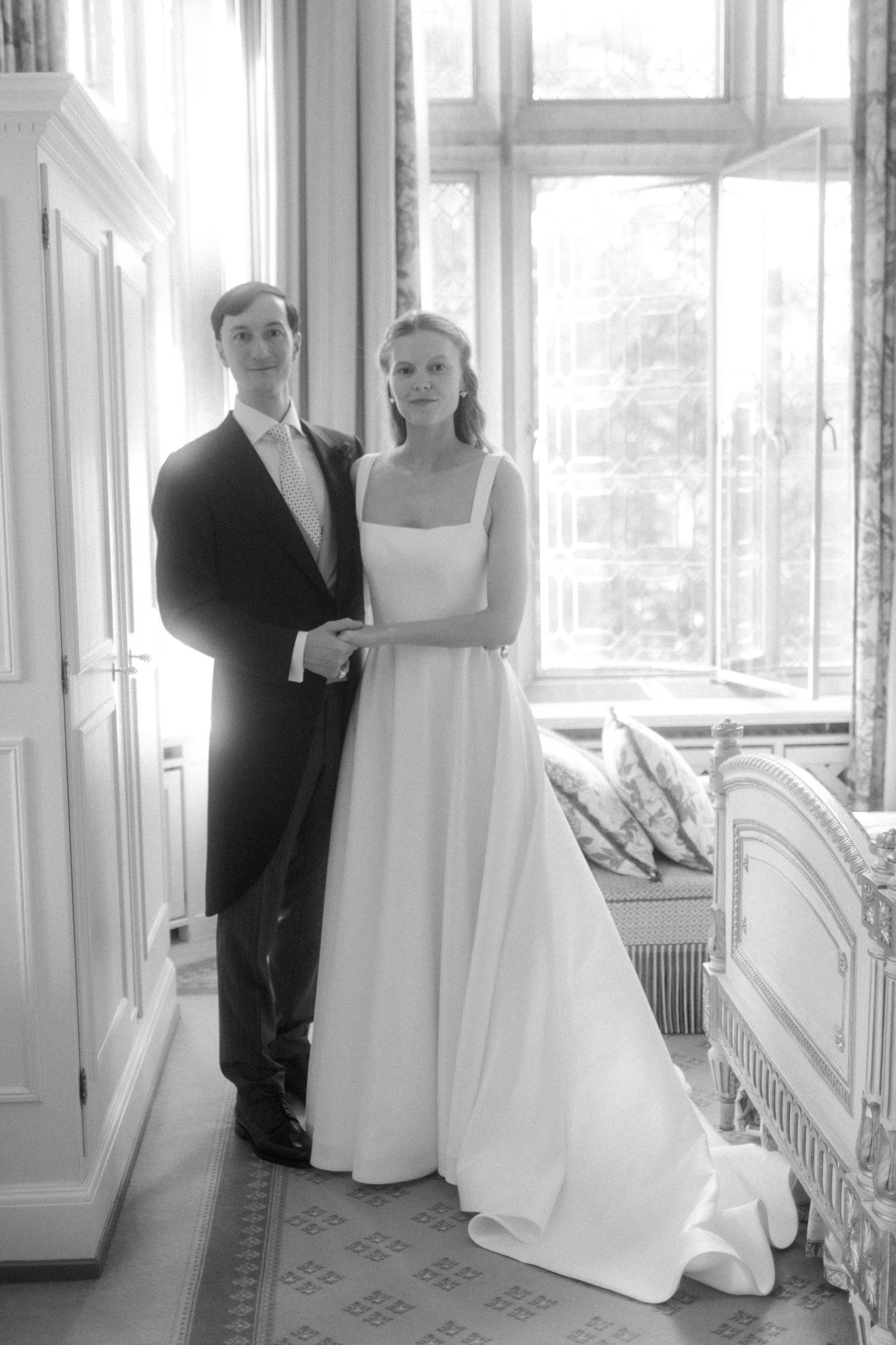 A formal portrait in a bright, elegant room with classic decor and large windows.