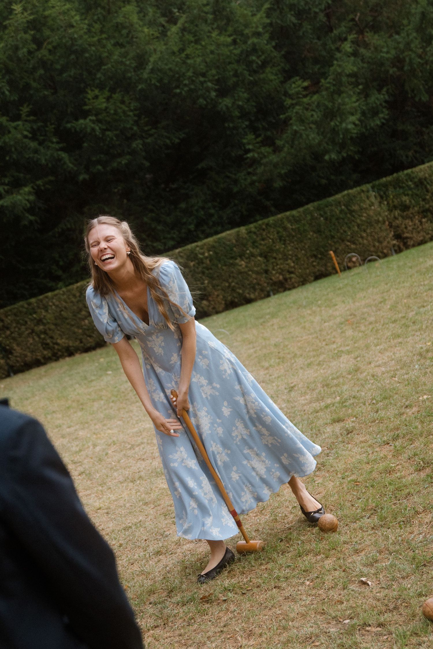 Person in a blue dress swinging a croquet mallet during an outdoor game.