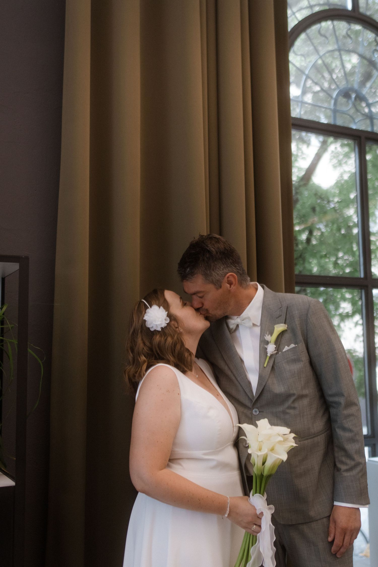 Wedding couple shares tender moments in front of large windows with dark curtains.