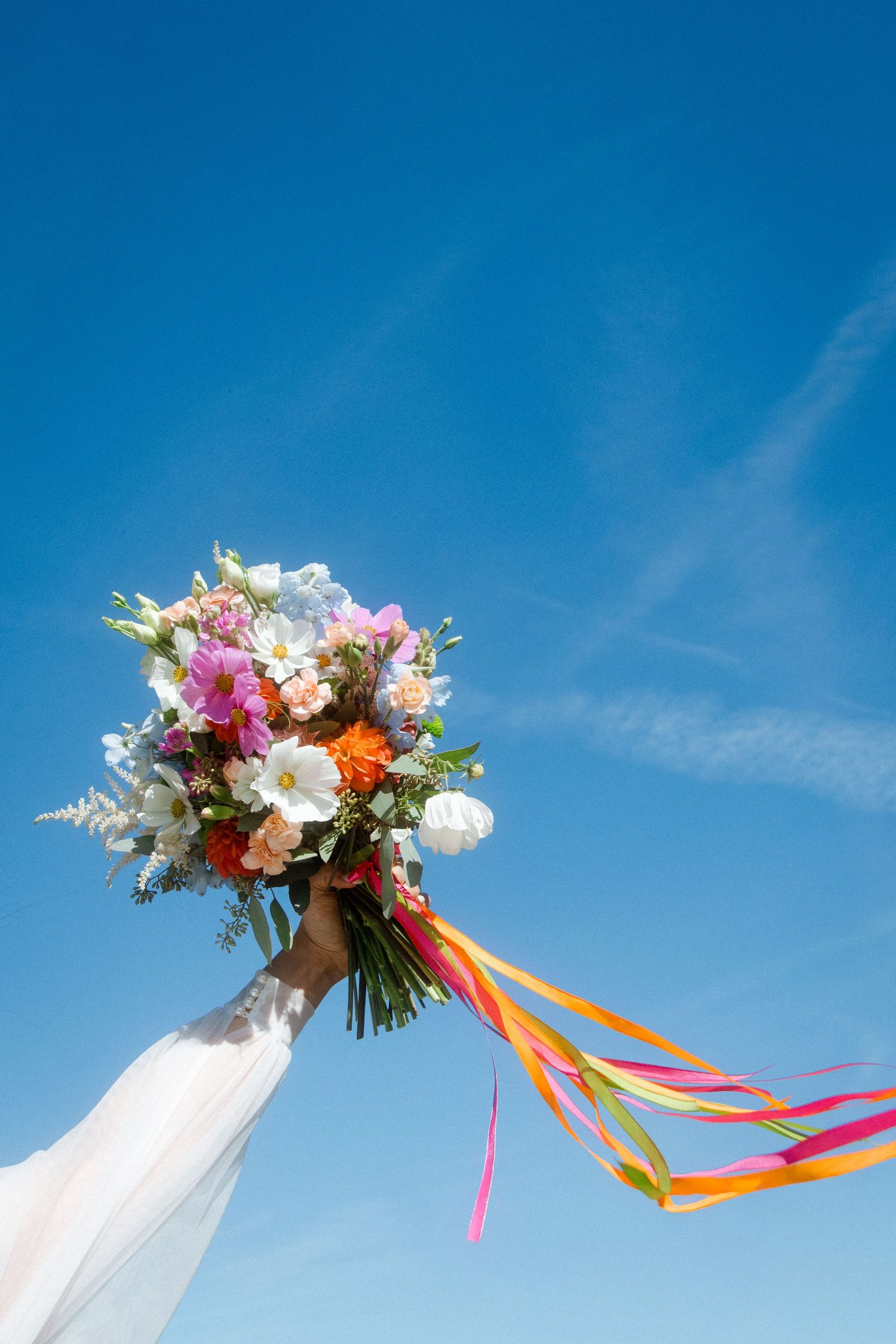 Colorful bridal bouquet with vibrant ribbons against bright blue sky.