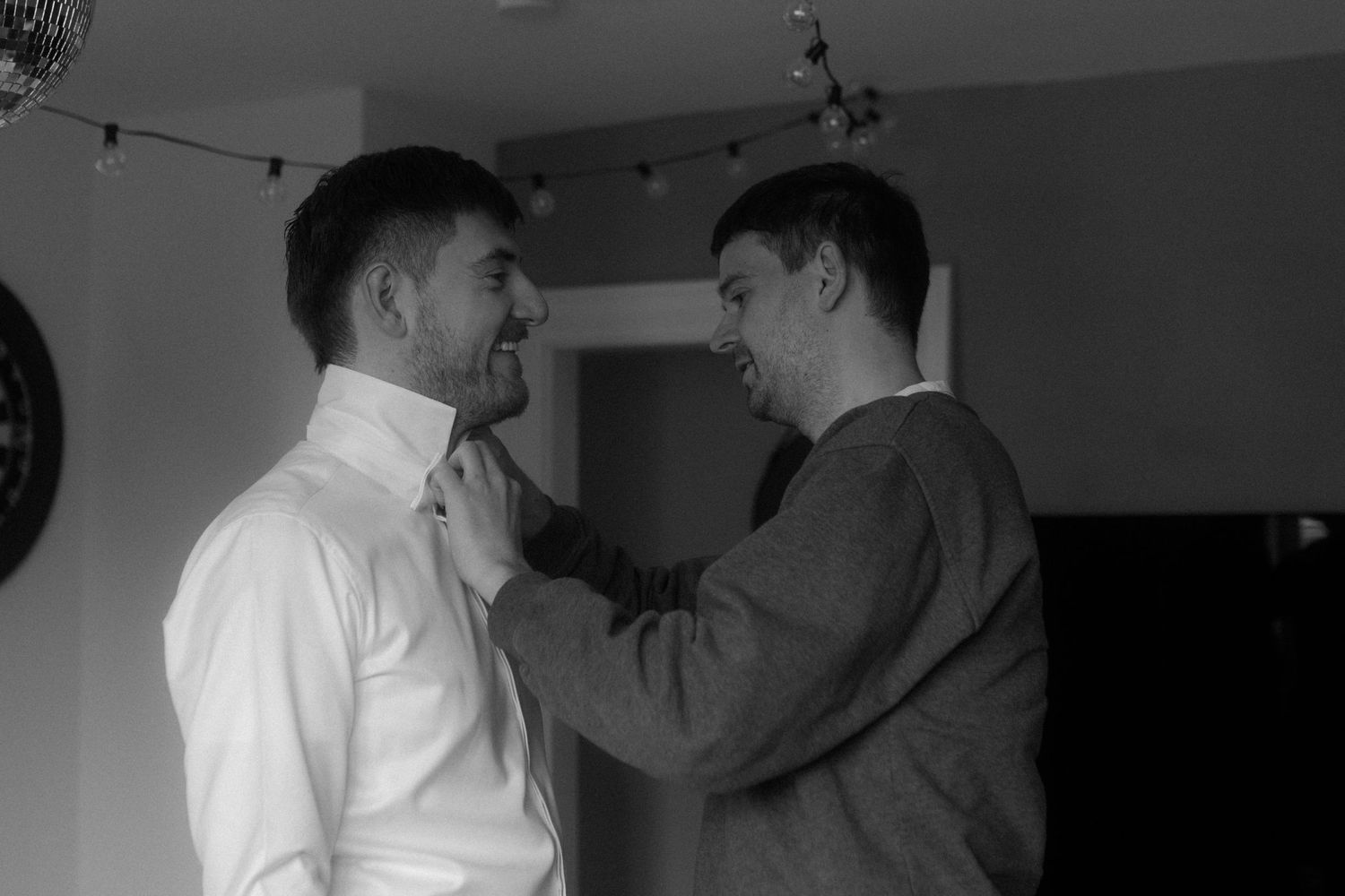 Two people sharing a tender moment while adjusting formal attire.