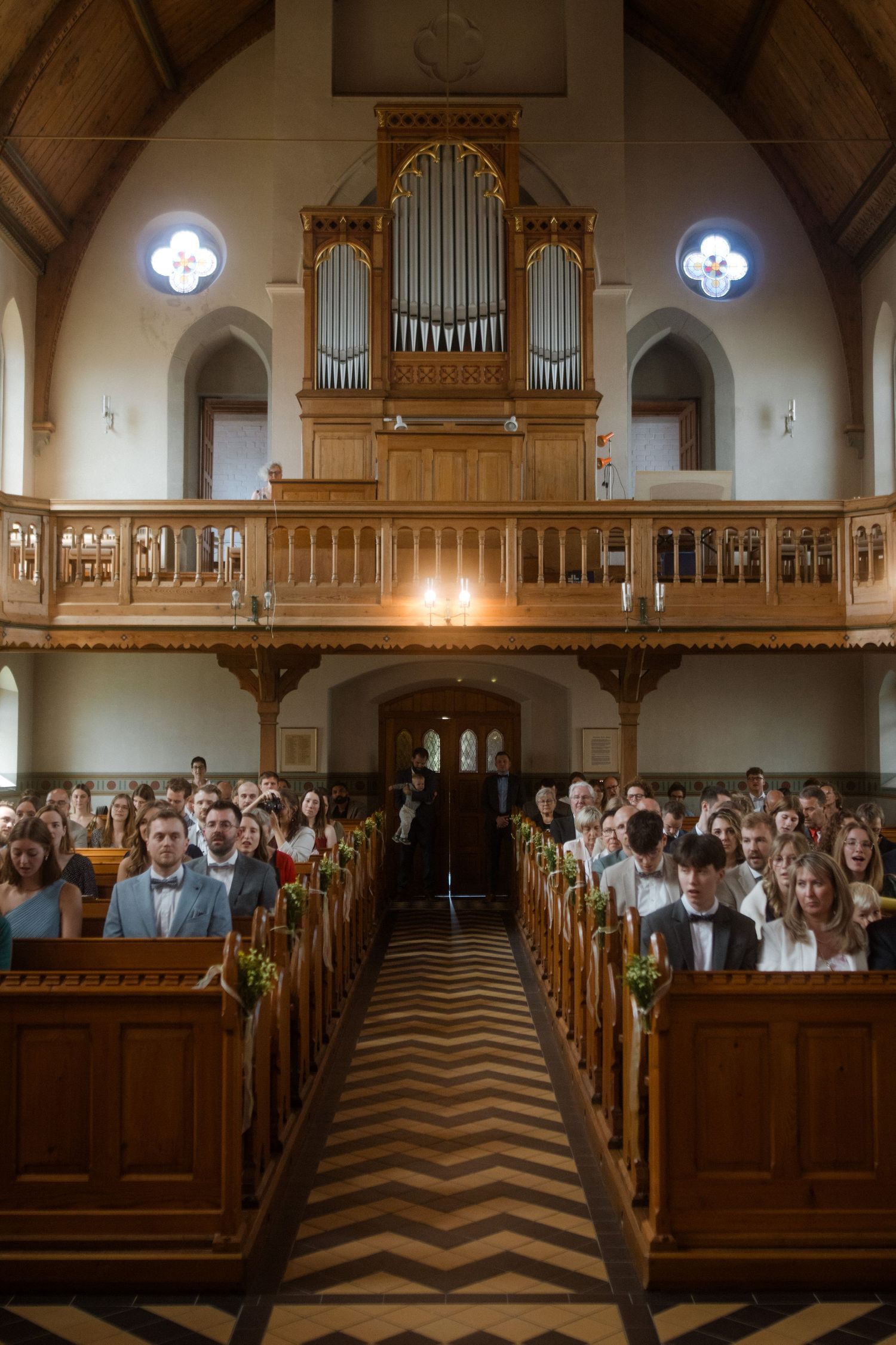 Interior of a church with wooden pews and pipe organ during a wedding ceremony.