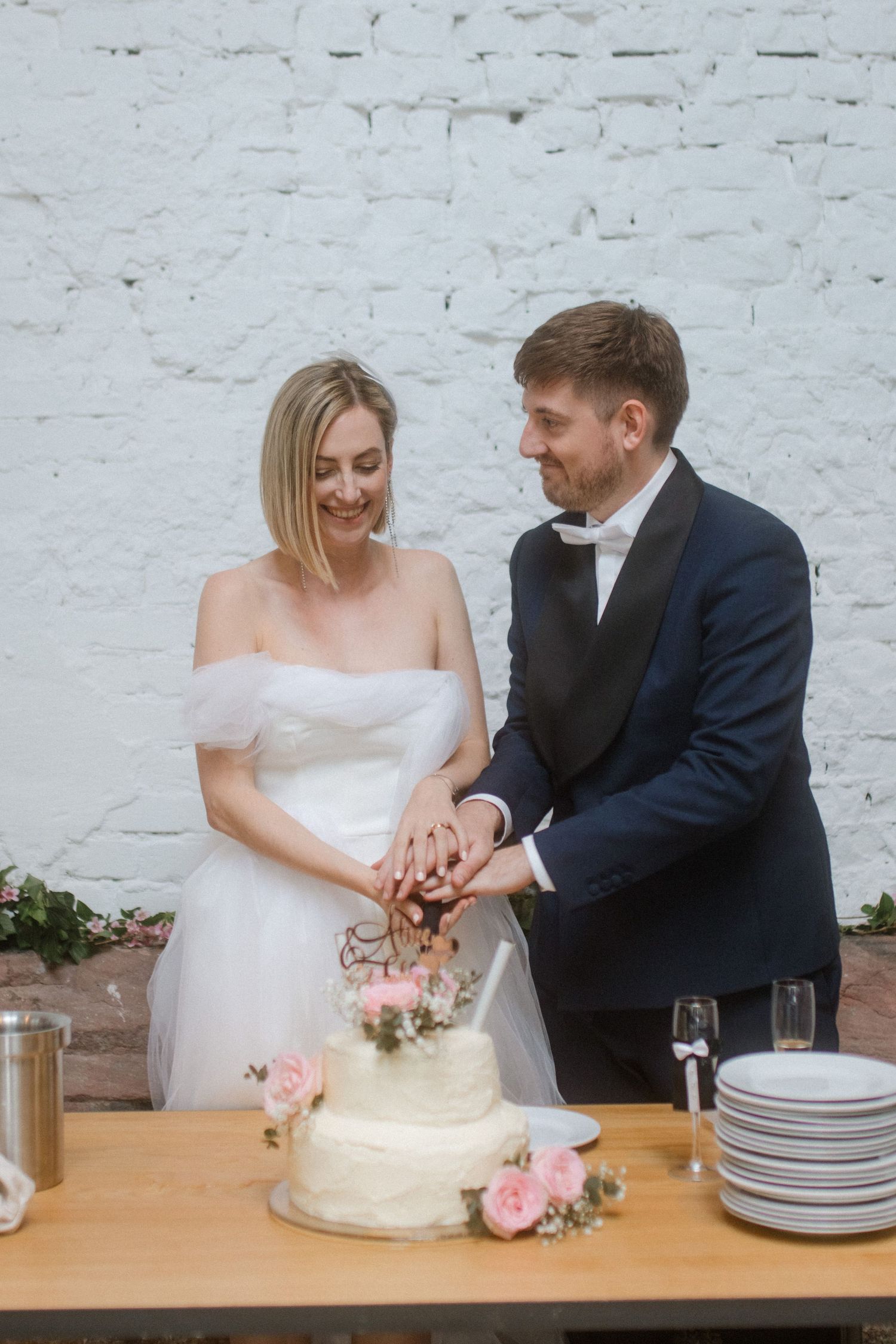 A couple cuts their wedding cake together at their reception against a white backdrop.