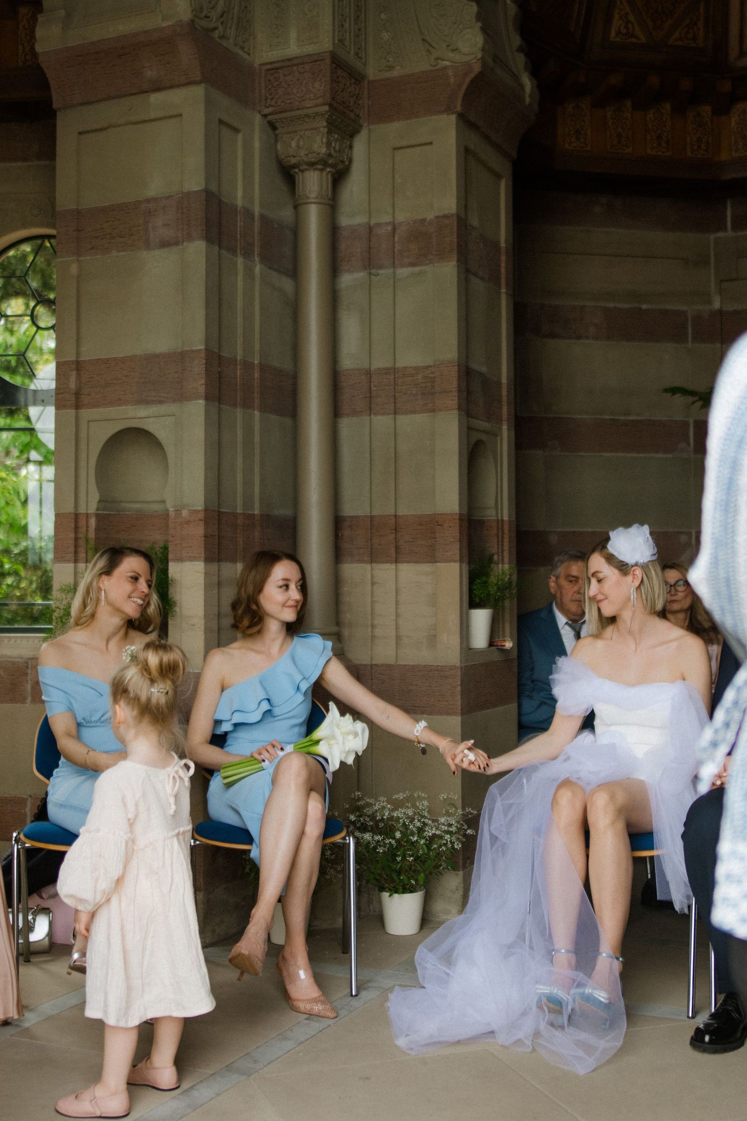 Wedding party sitting in an elegant columned venue with bridesmaids in light blue dresses.