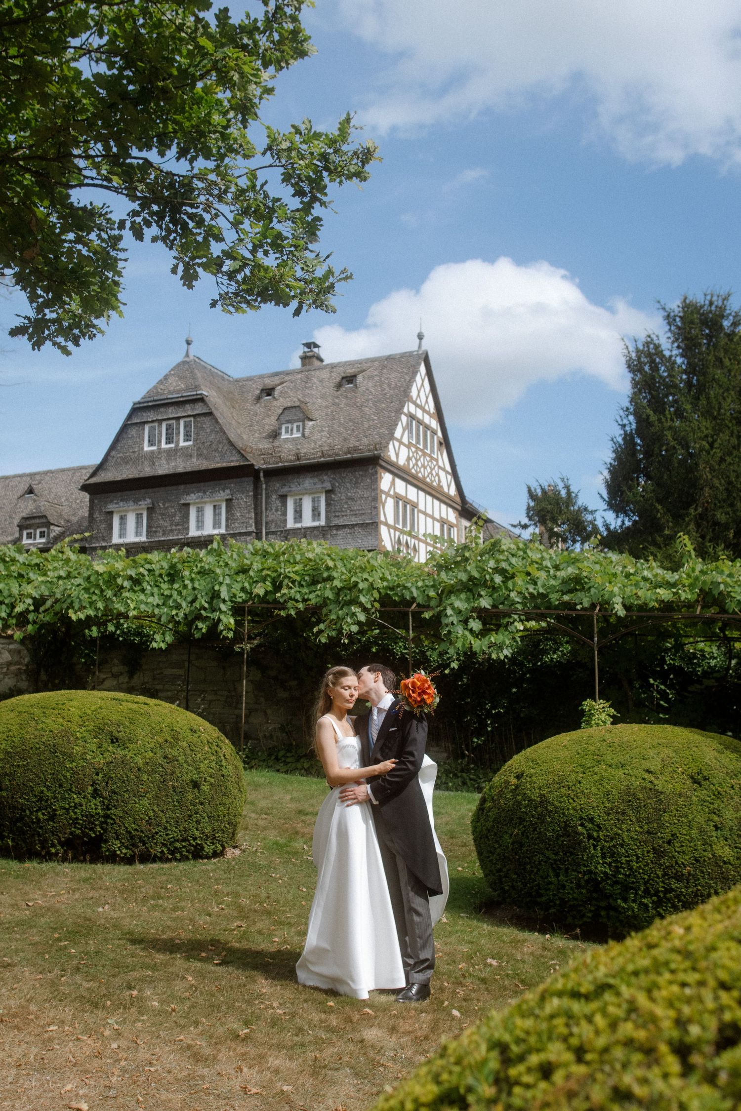 Wedding portraits taken in a sunny garden with a historic house in the background.