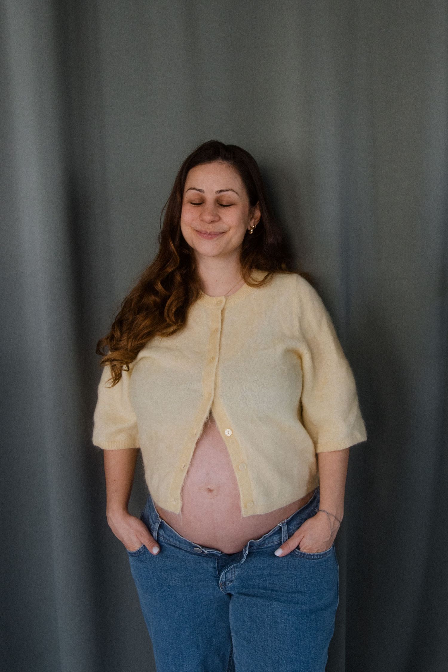 Person in cream colored cardigan and jeans posing against a grey backdrop in various casual poses.