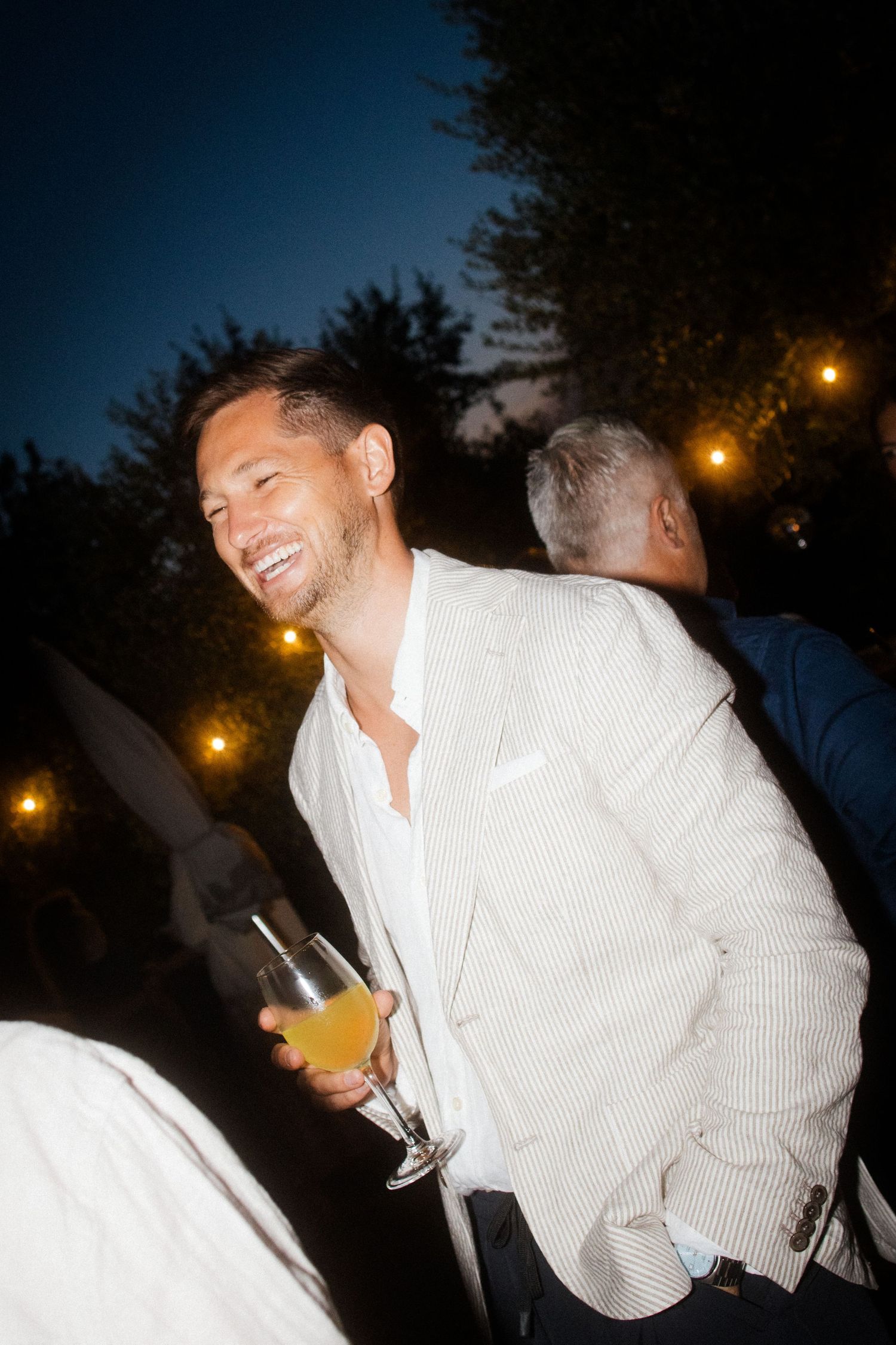 A person in white laughing joyfully during an evening celebration.