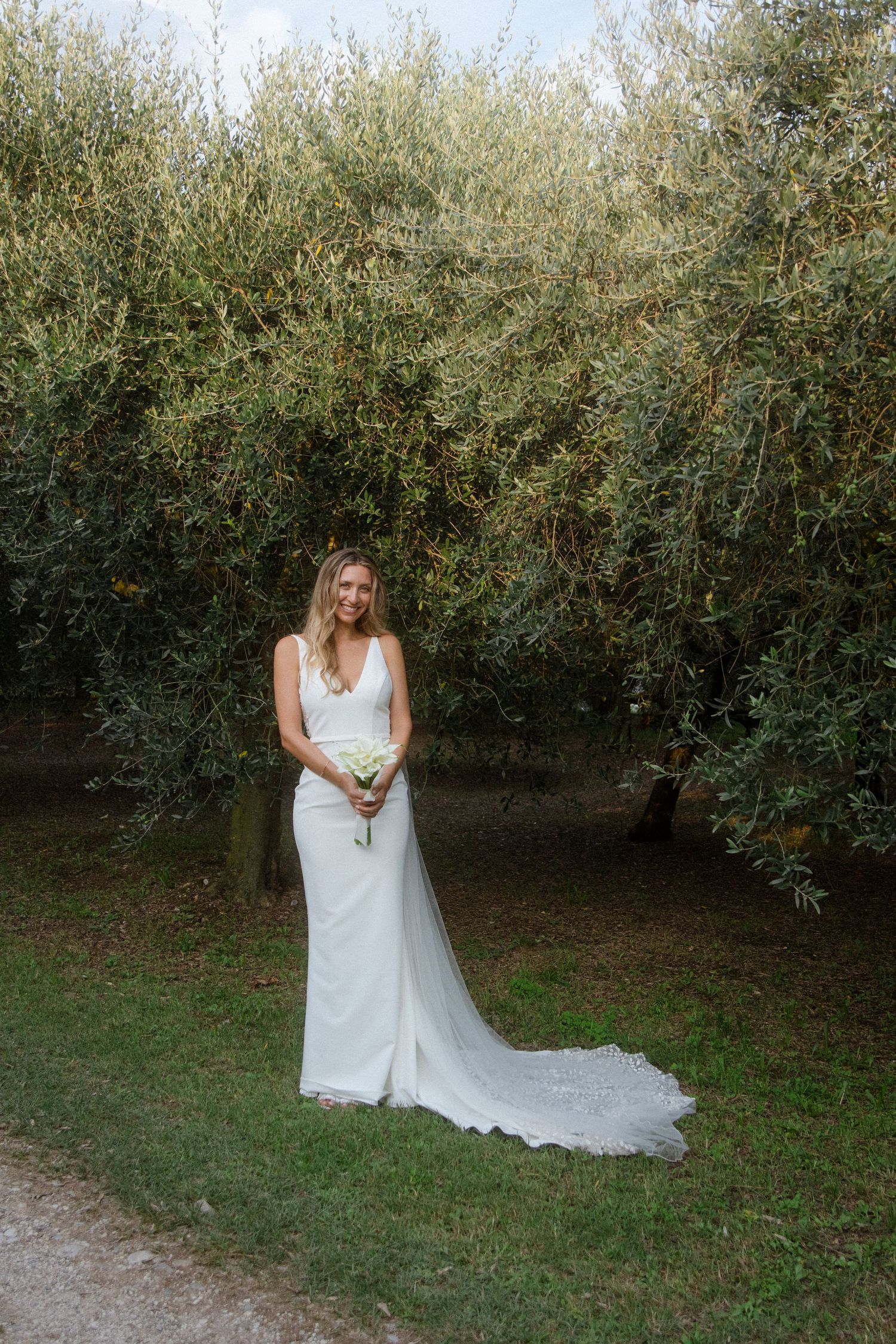 Bride in a sleek white gown poses against a backdrop of lush garden foliage.