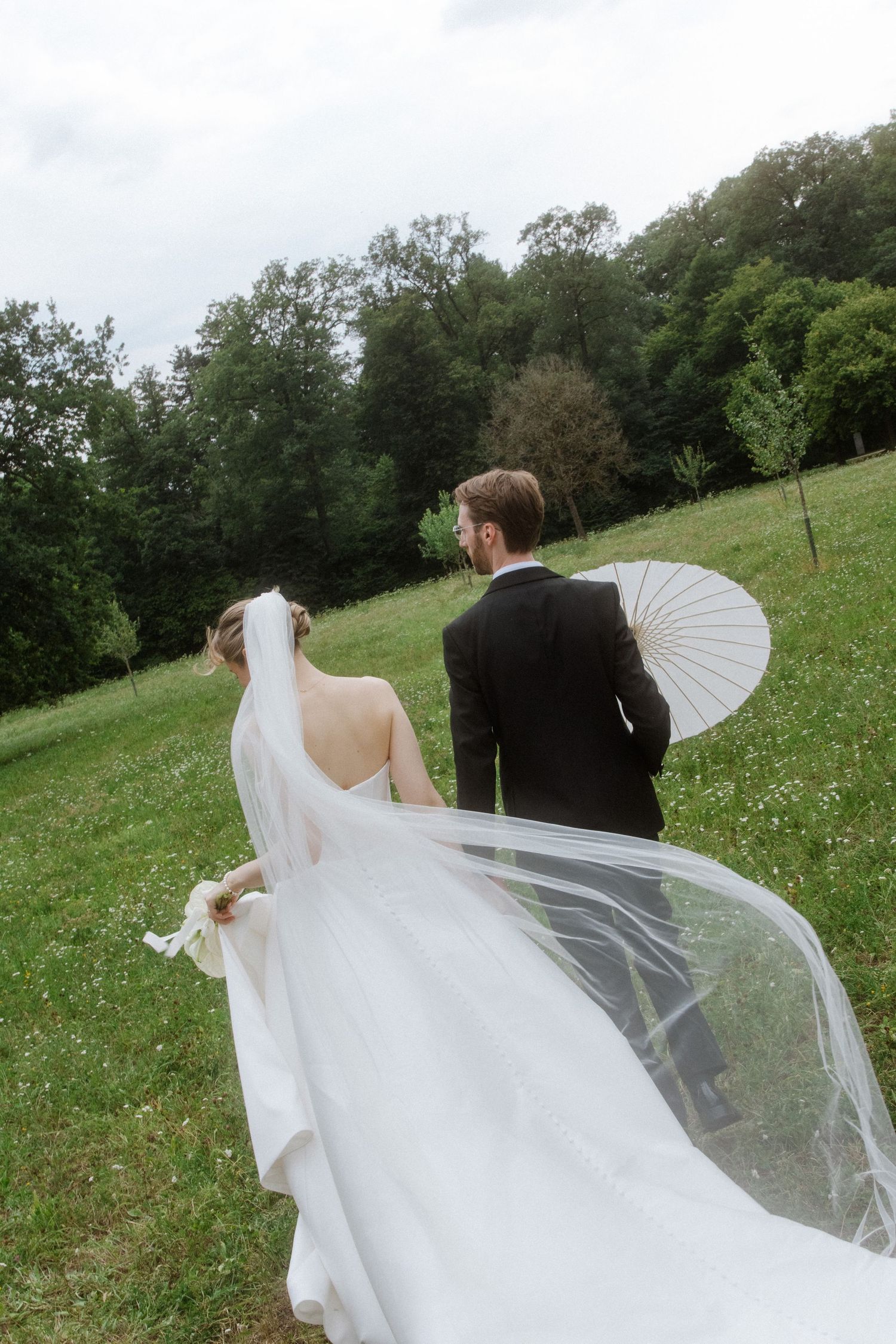 A flowing white wedding dress and veil catch the breeze in a meadow.