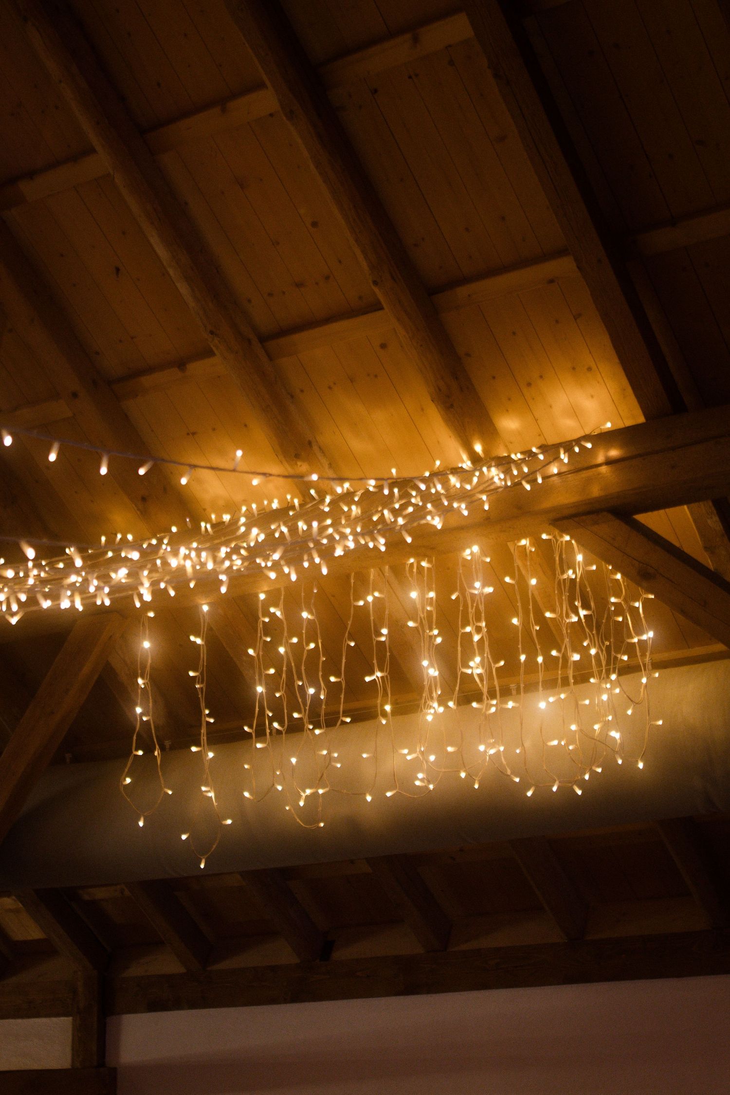 Warm fairy lights hanging from wooden rafters create a magical atmosphere in rustic venue.