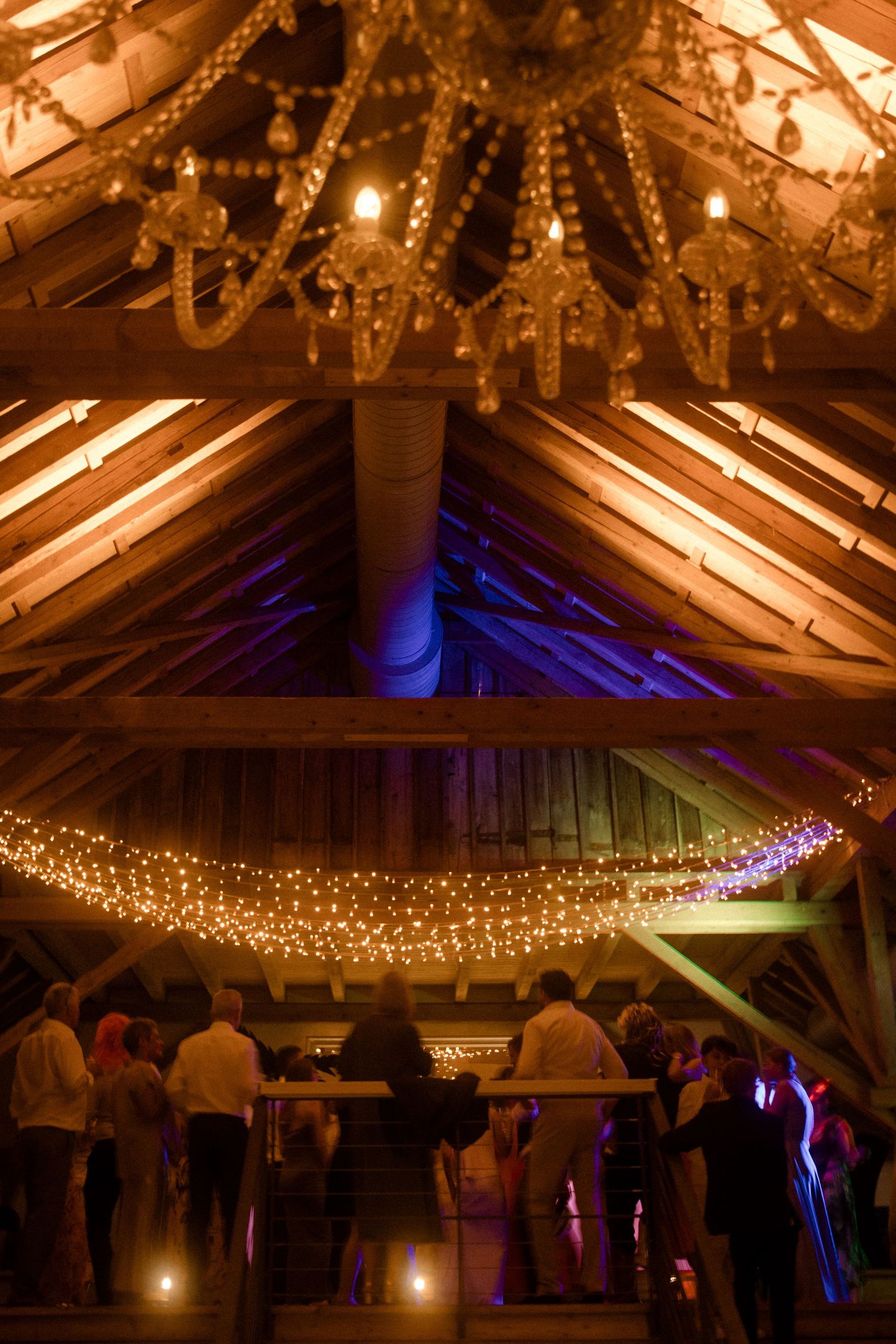 Rustic barn venue decorated with warm string lights and chandelier for evening event.