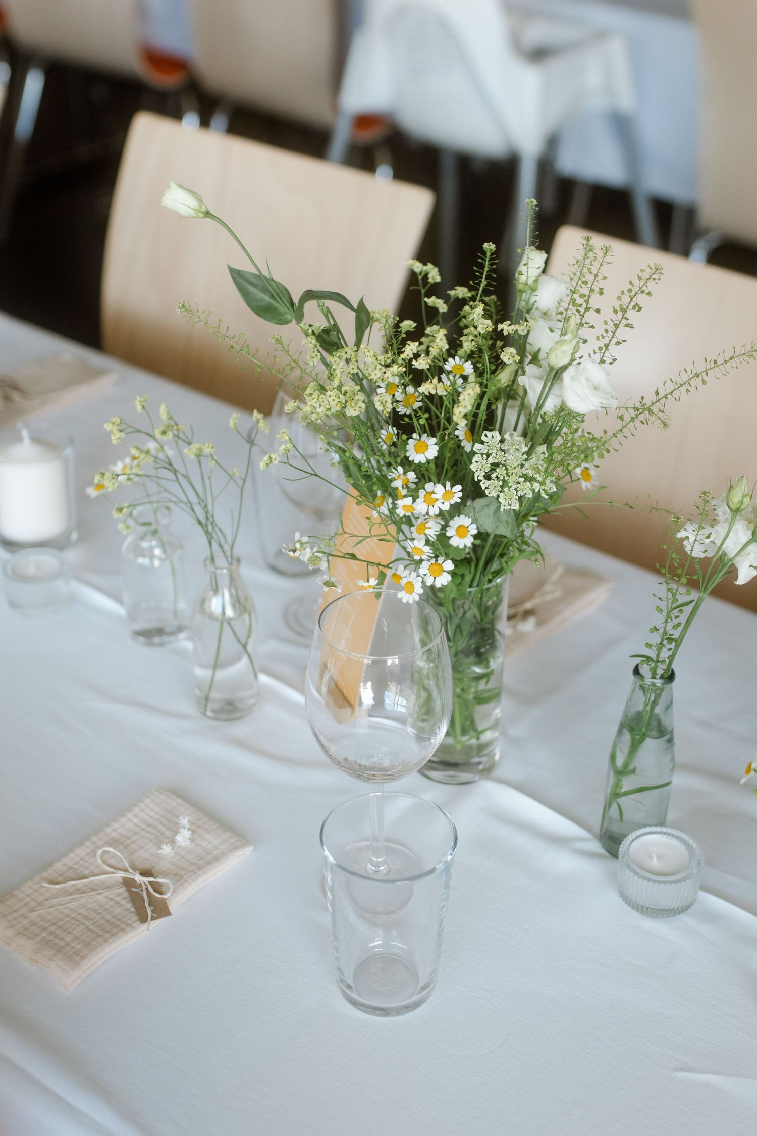 Elegant table setting with wildflower centerpieces in glass vases on white tablecloth for a wedding reception.