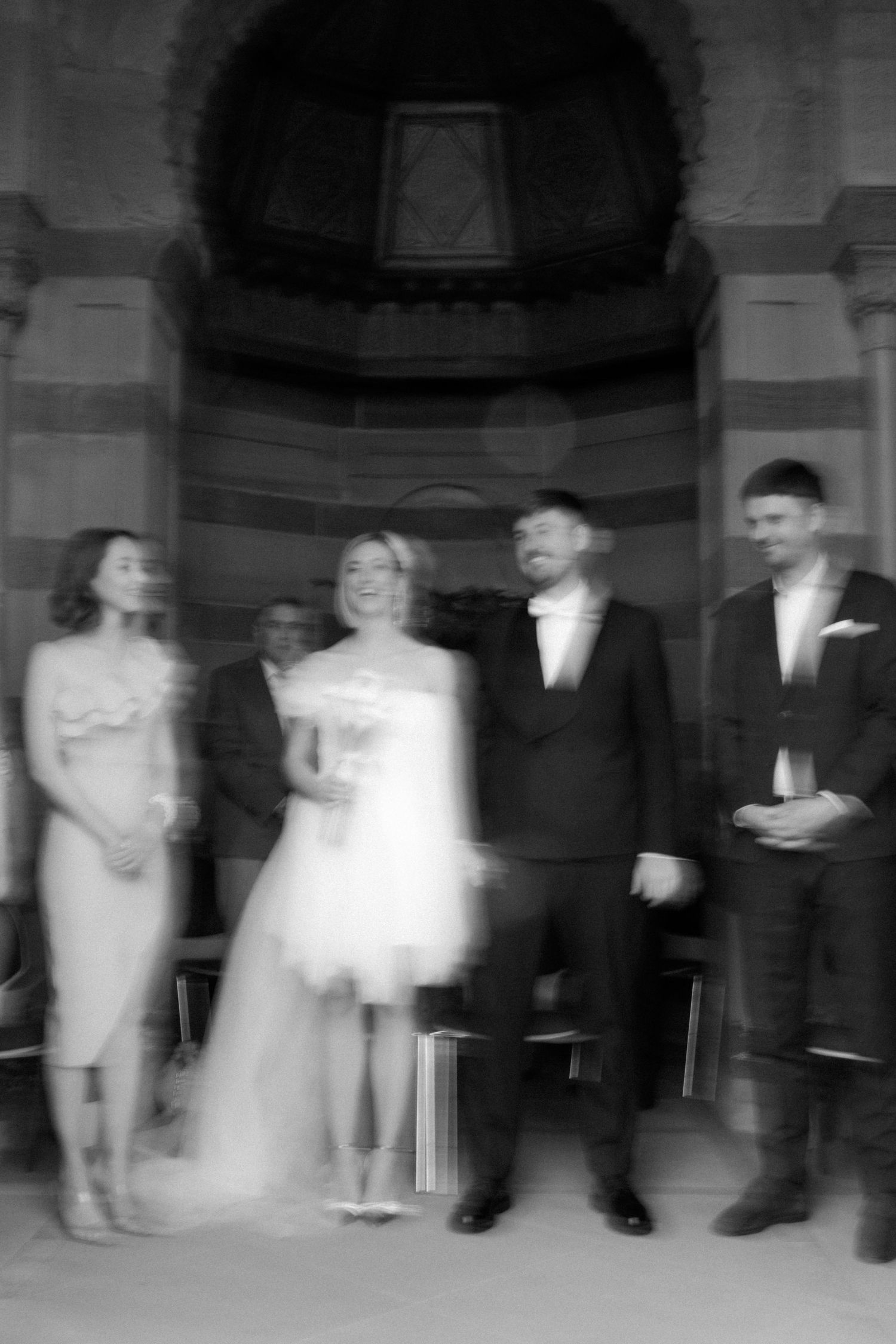 Black and white vintage wedding party photo showing bridal group beneath ornate archway.