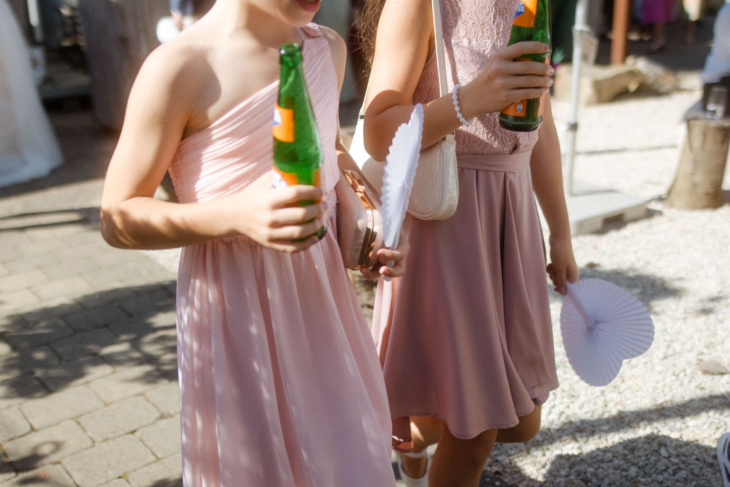 Wedding guests in pink dresses holding beverages on a sunny outdoor patio.