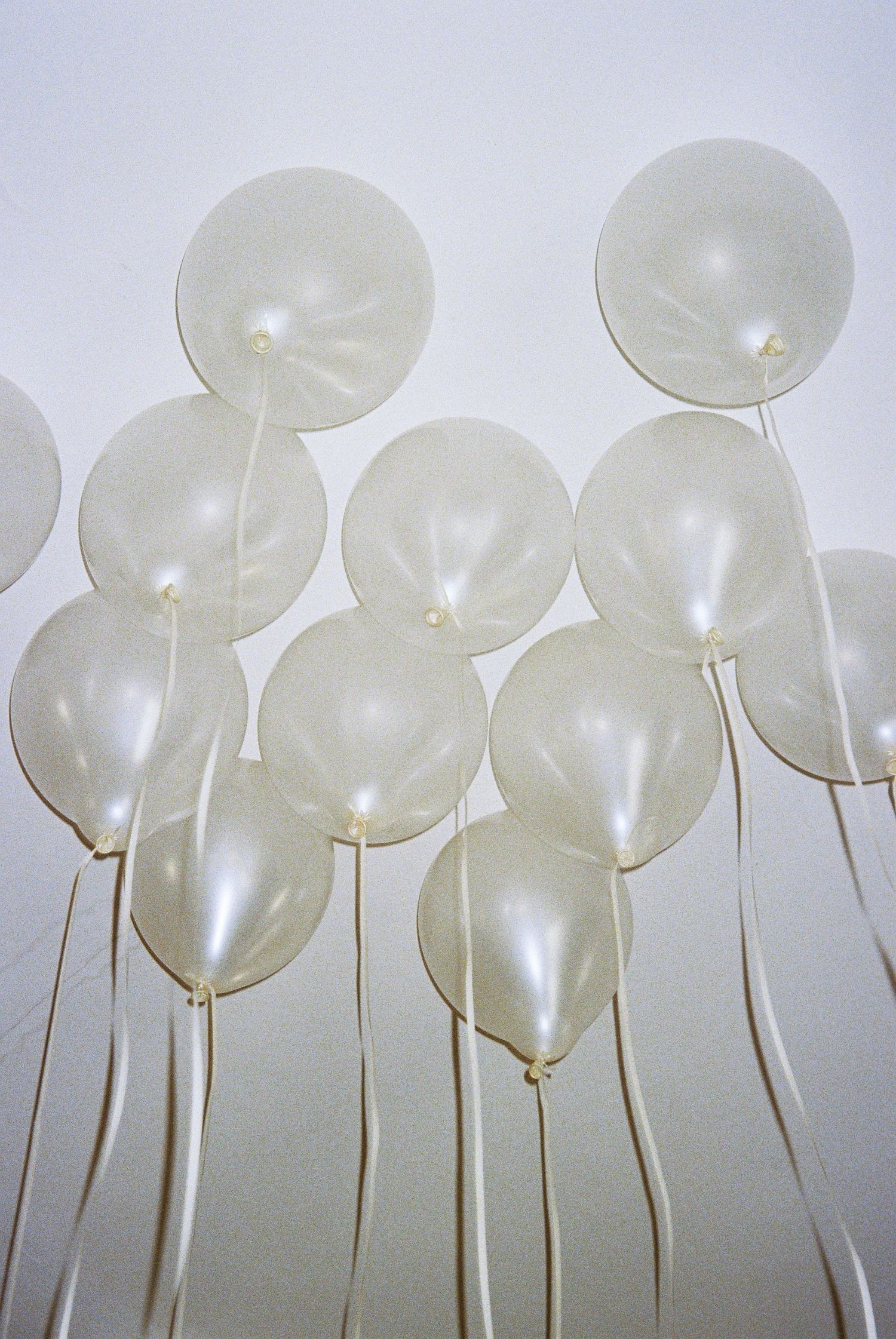 Row of white balloons floating upward against a light background creating an ethereal artistic installation.
