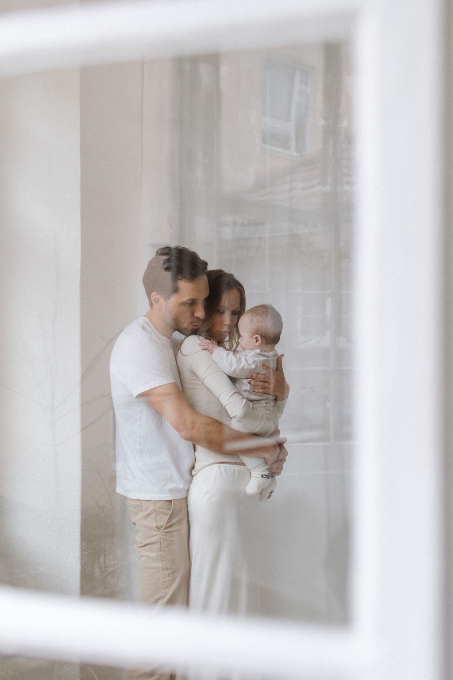 Family sharing tender moments together in a bright, airy room with white curtains.