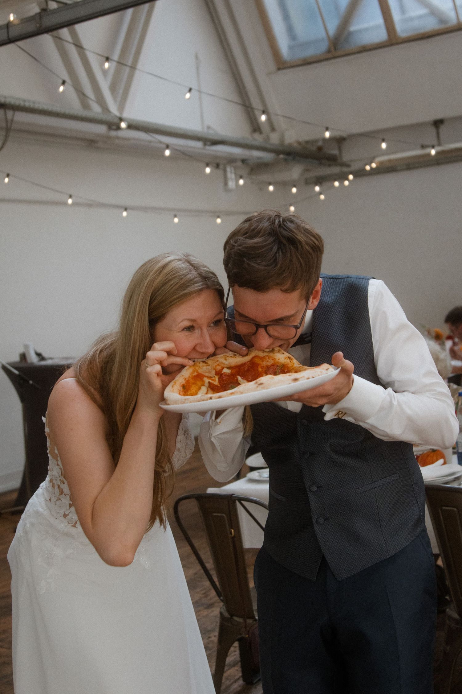 Couple sharing a slice of pizza together at their wedding reception.