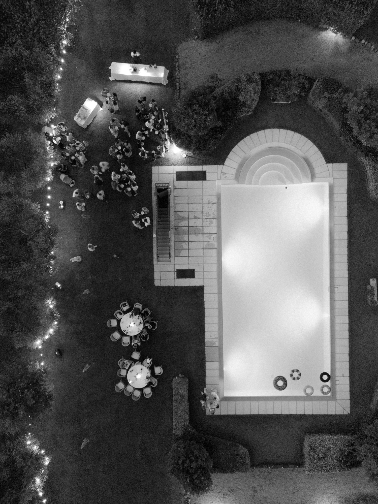 Aerial view of a white tent structure and outdoor event space at night with glowing lights.
