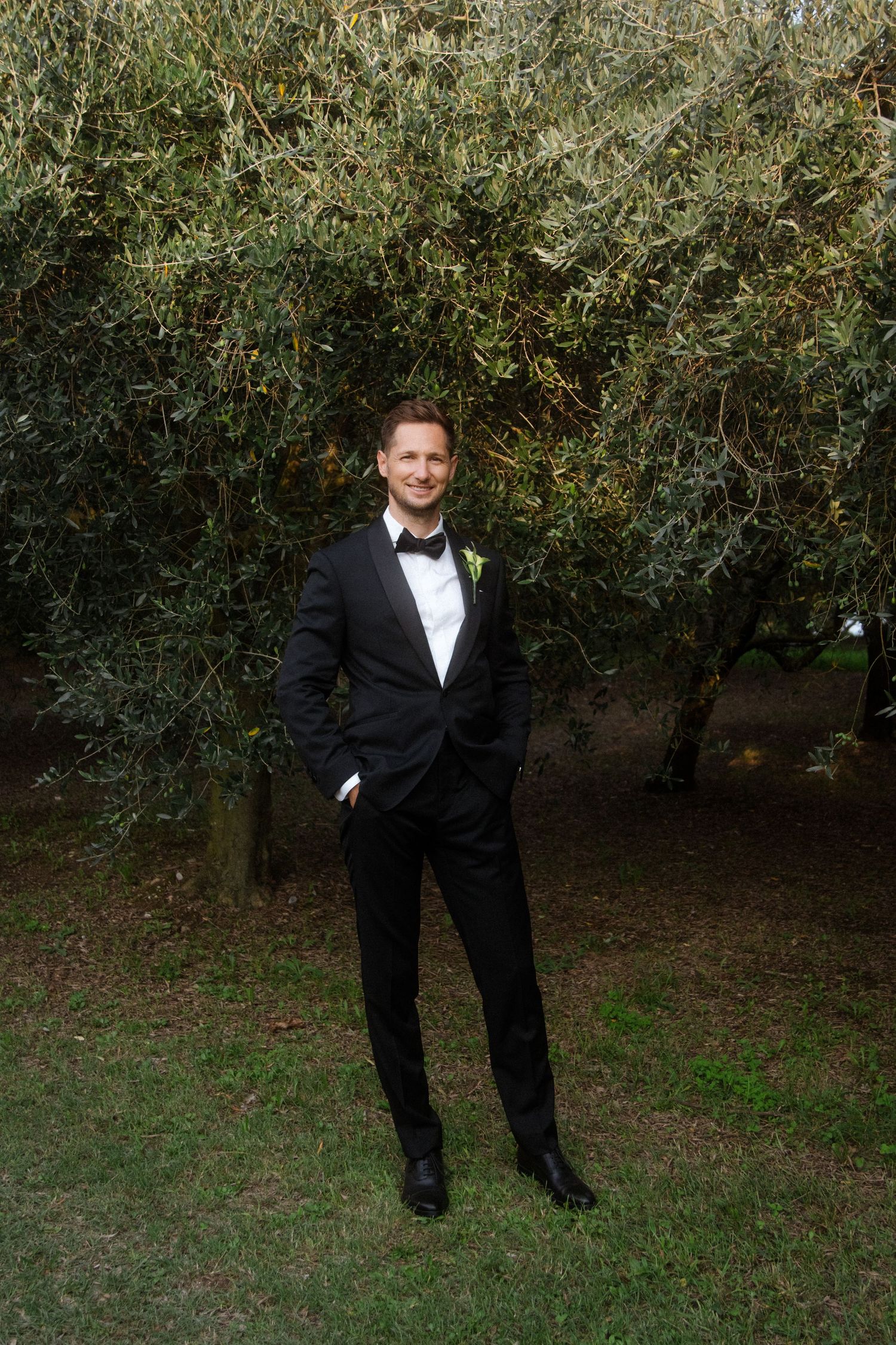 A formal wedding photo shoot in an outdoor garden setting with olive trees.