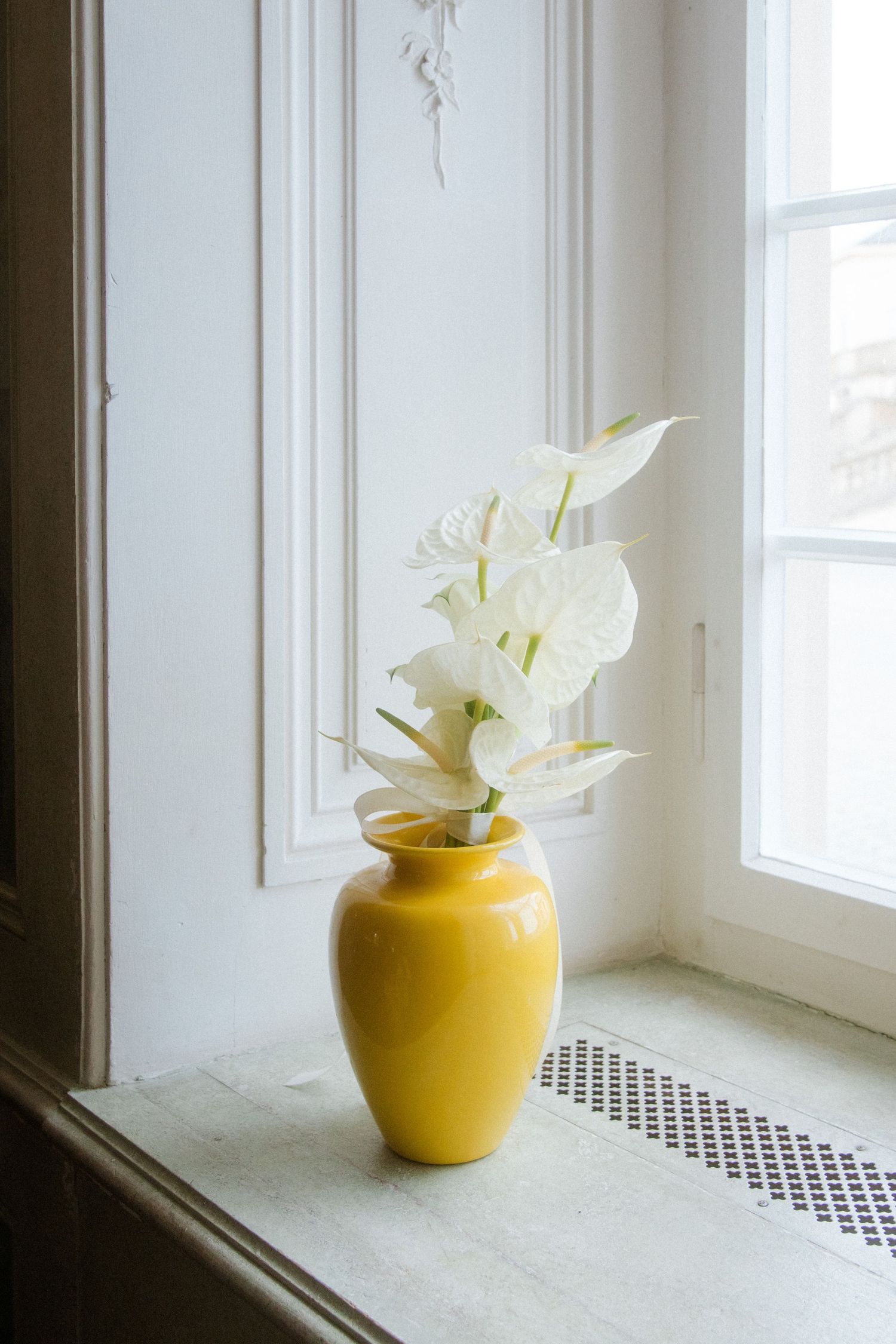 Yellow ceramic vase with white calla lilies displayed on a bright windowsill.