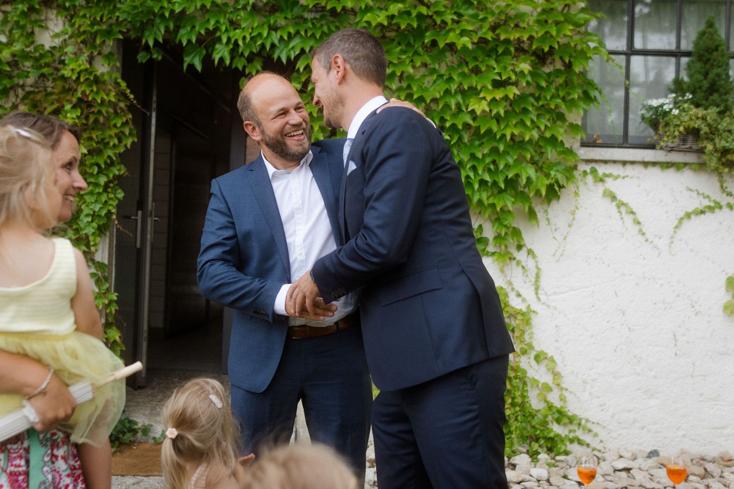 Guests chatting during outdoor wedding reception near ivy-covered wall.