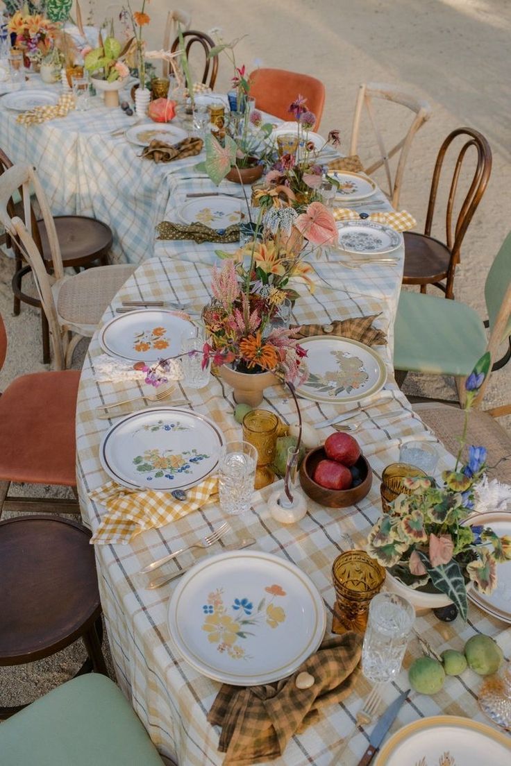 Elegant outdoor table setting with mismatched vintage plates and colorful floral centerpieces.