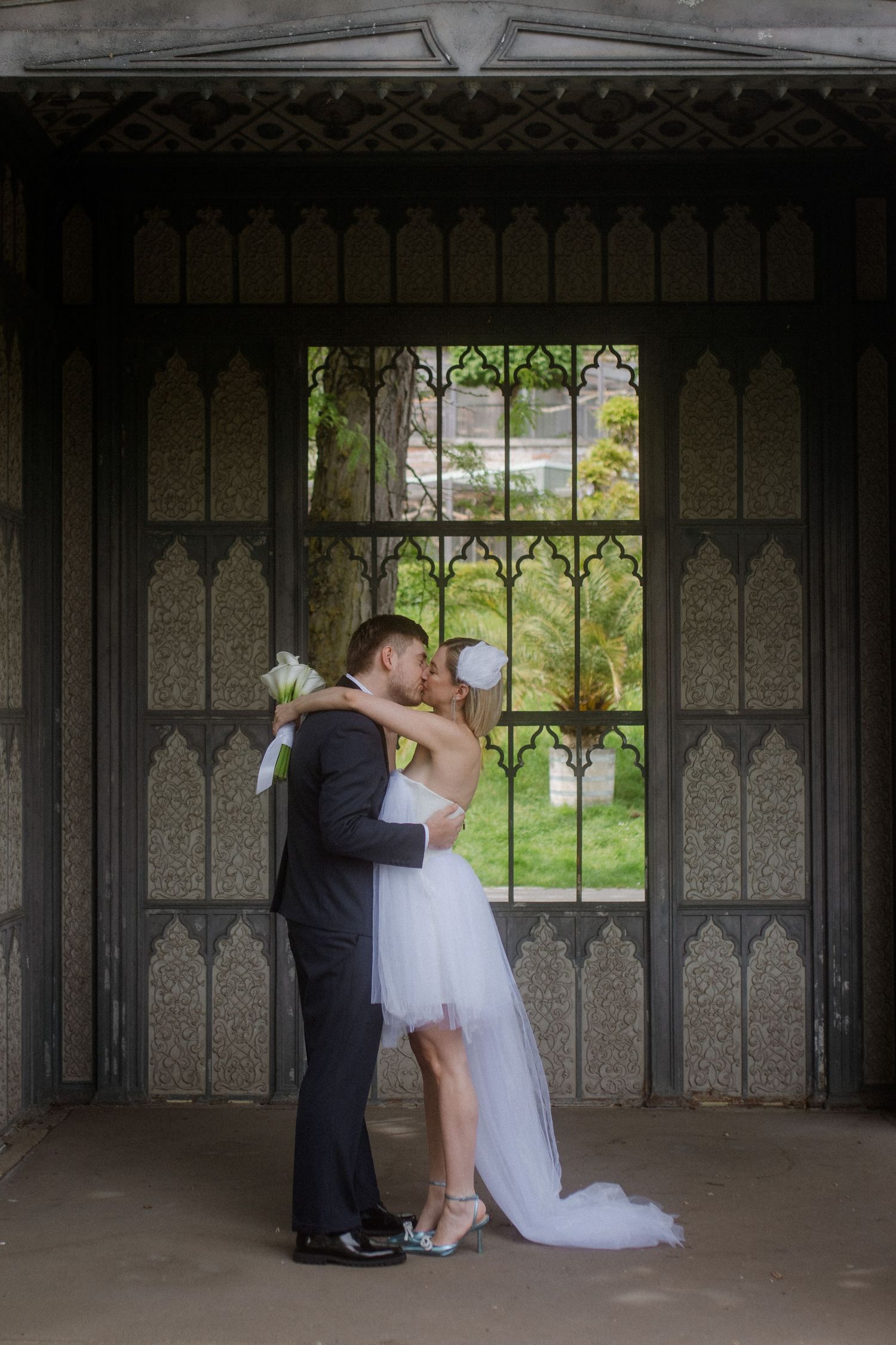 Romantic wedding couple embracing in front of a Gothic-style window frame.