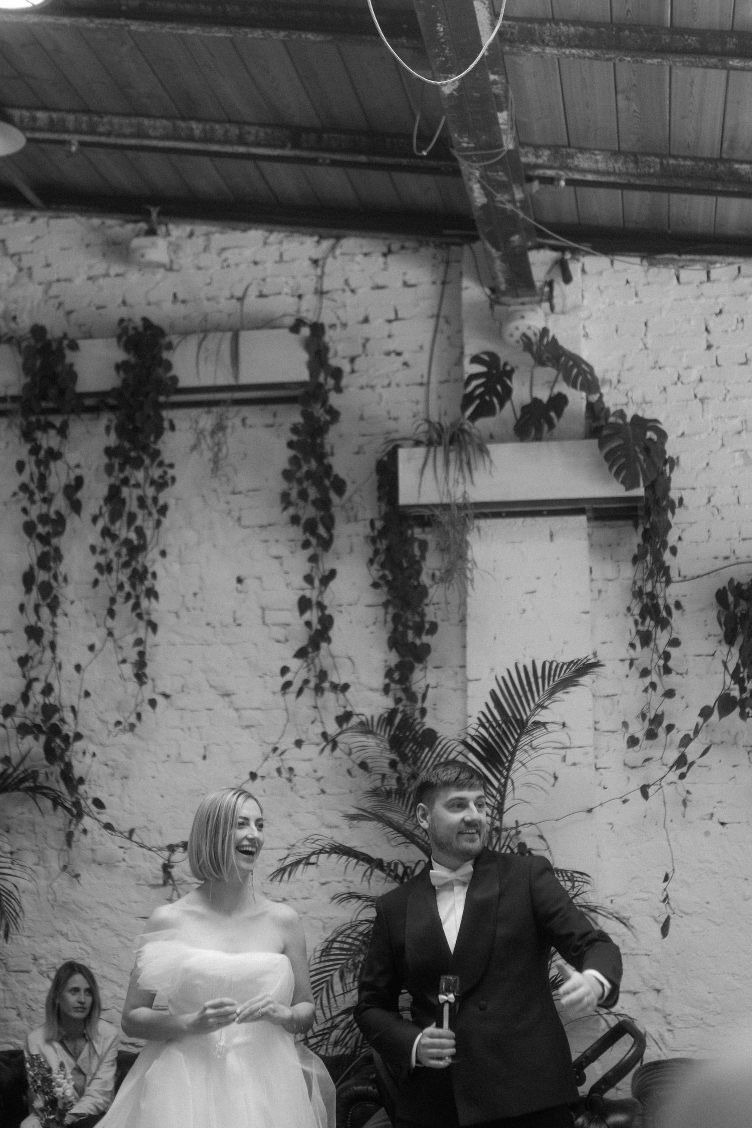 A couple celebrates during their wedding reception in a venue with exposed brick and hanging plants.