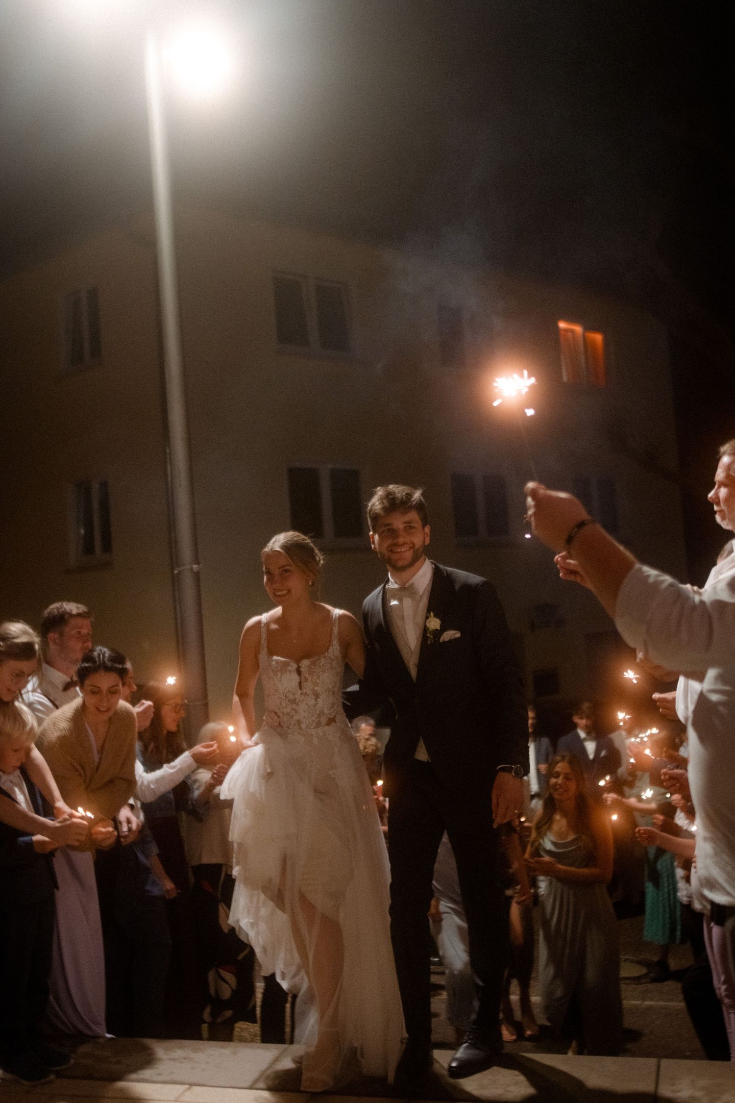 A romantic sparkler send-off during a nighttime wedding with guests lining the pathway.