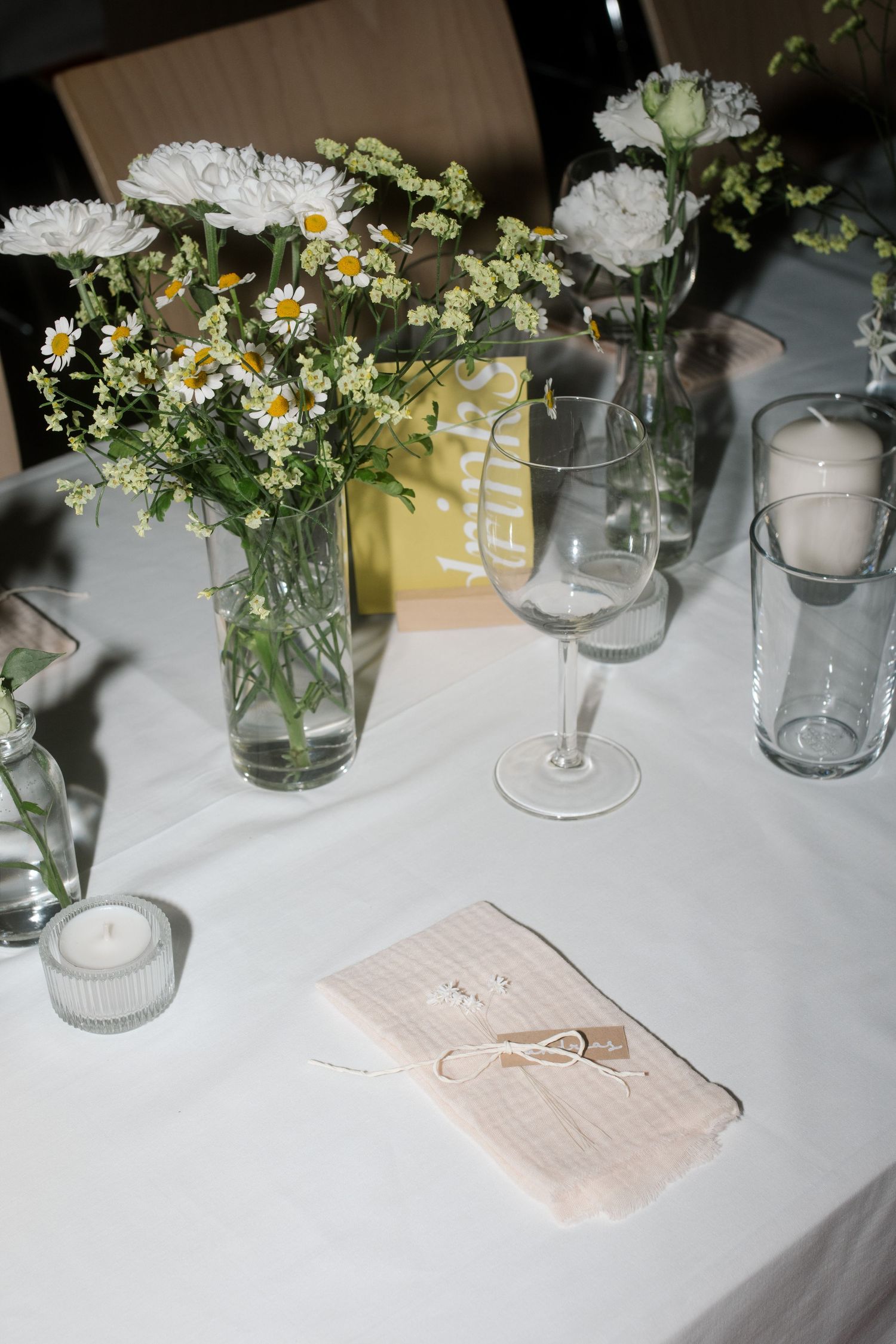 Wedding table setting with white carnations and daisies in glass vases next to menu cards.