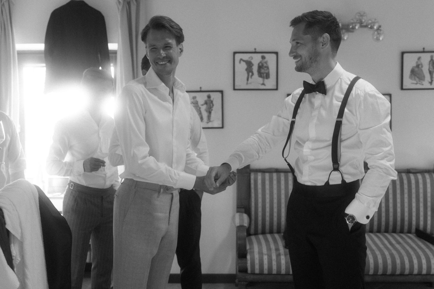 People in white shirts and suspenders interact in a vintage-styled room with striped wallpaper.