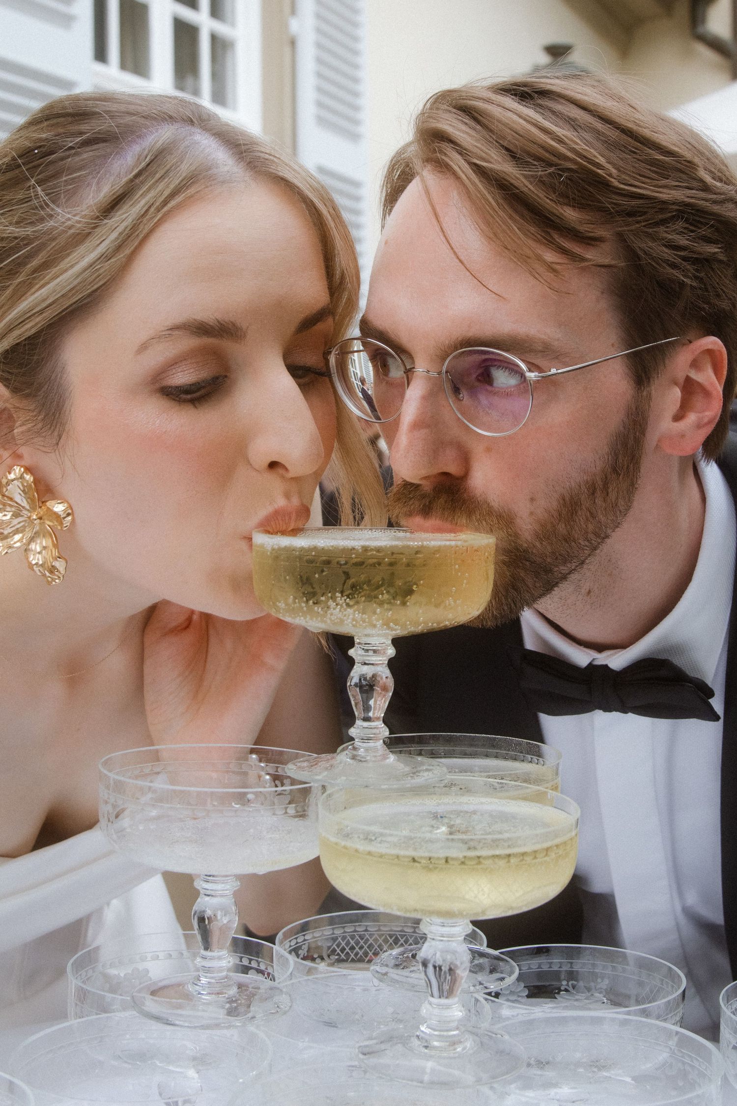 A couple drinking champagne from a tower of glasses at their wedding.