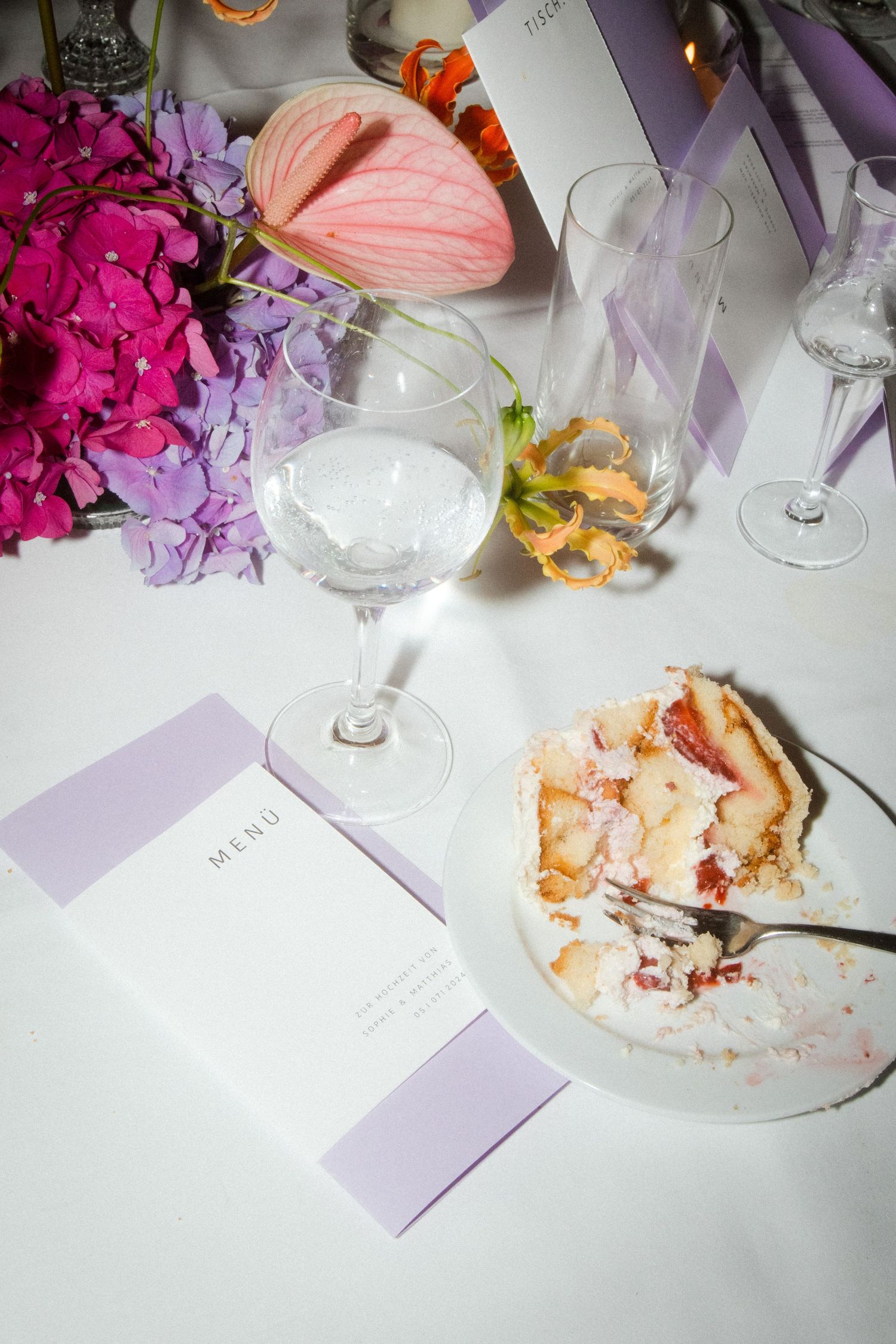 An elegant place setting with menu card, wine glass, and partially eaten cake slice.
