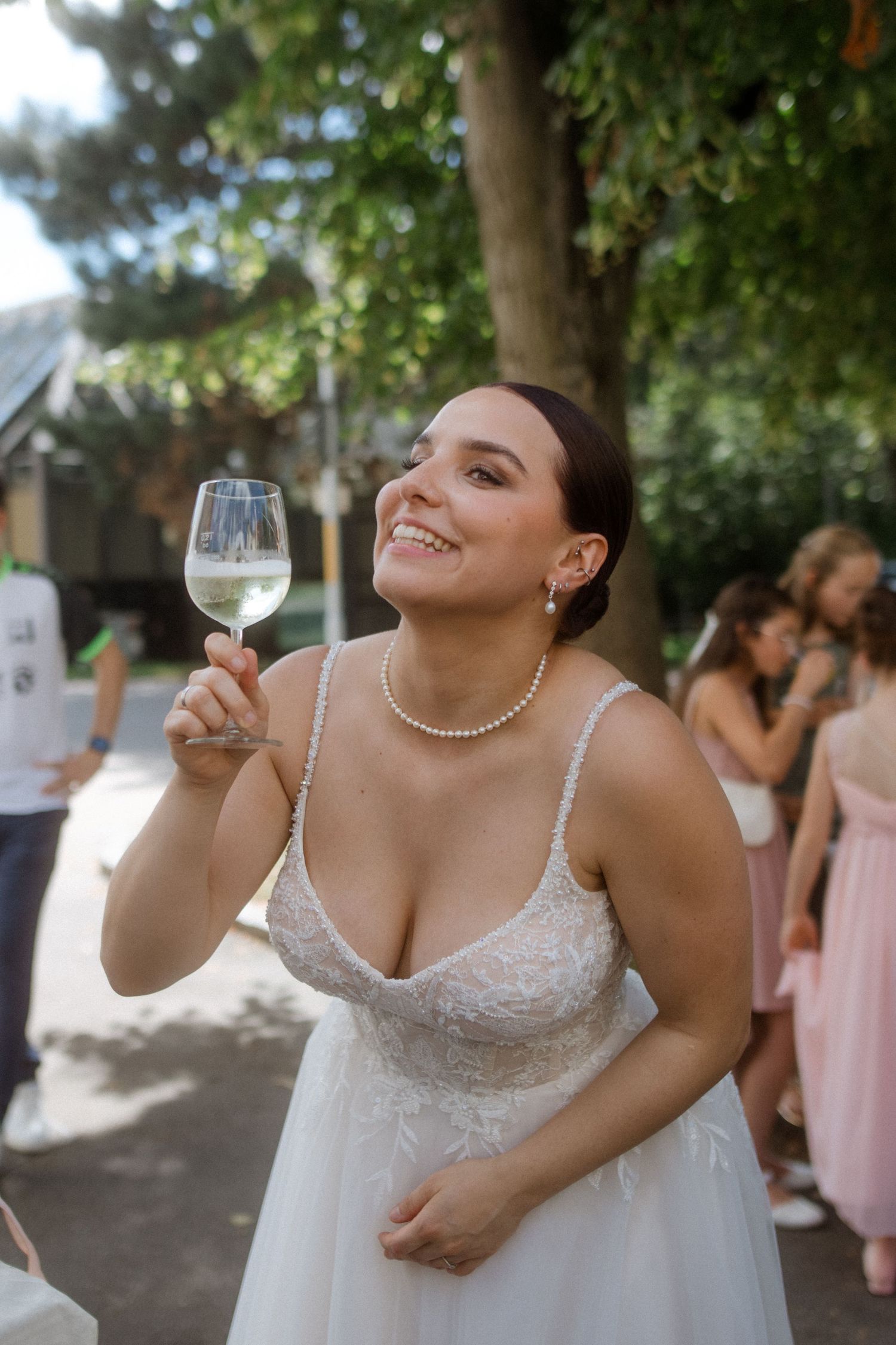 A bride in a white dress holds a wine glass while celebrating at an outdoor reception.