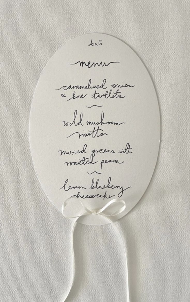Handwritten wedding menu on oval paper tag with white ribbon.